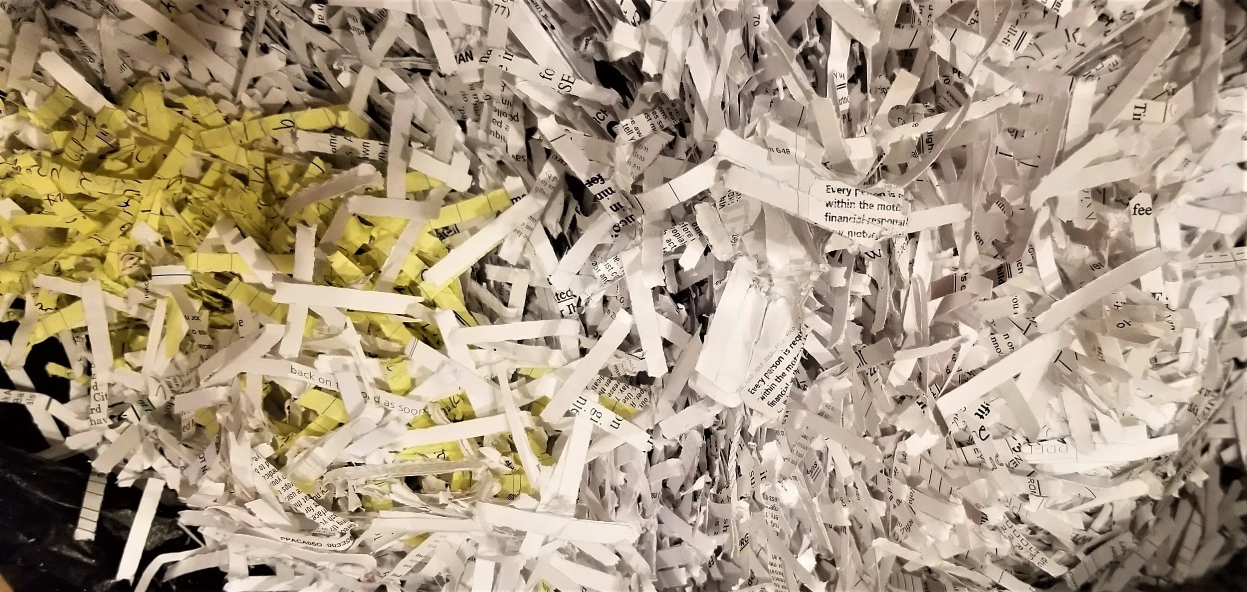 A pile of shredded paper, mostly white with some yellow pieces, mixed together with visible text on the torn pages.