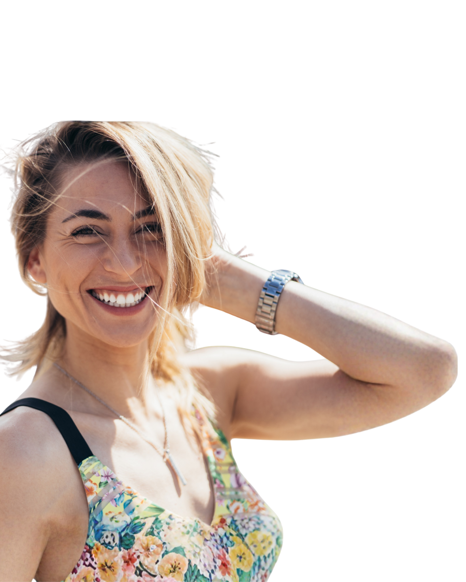 A smiling woman with blonde hair, wearing a colorful floral top, a watch, and a necklace, outdoors in bright sunlight.
