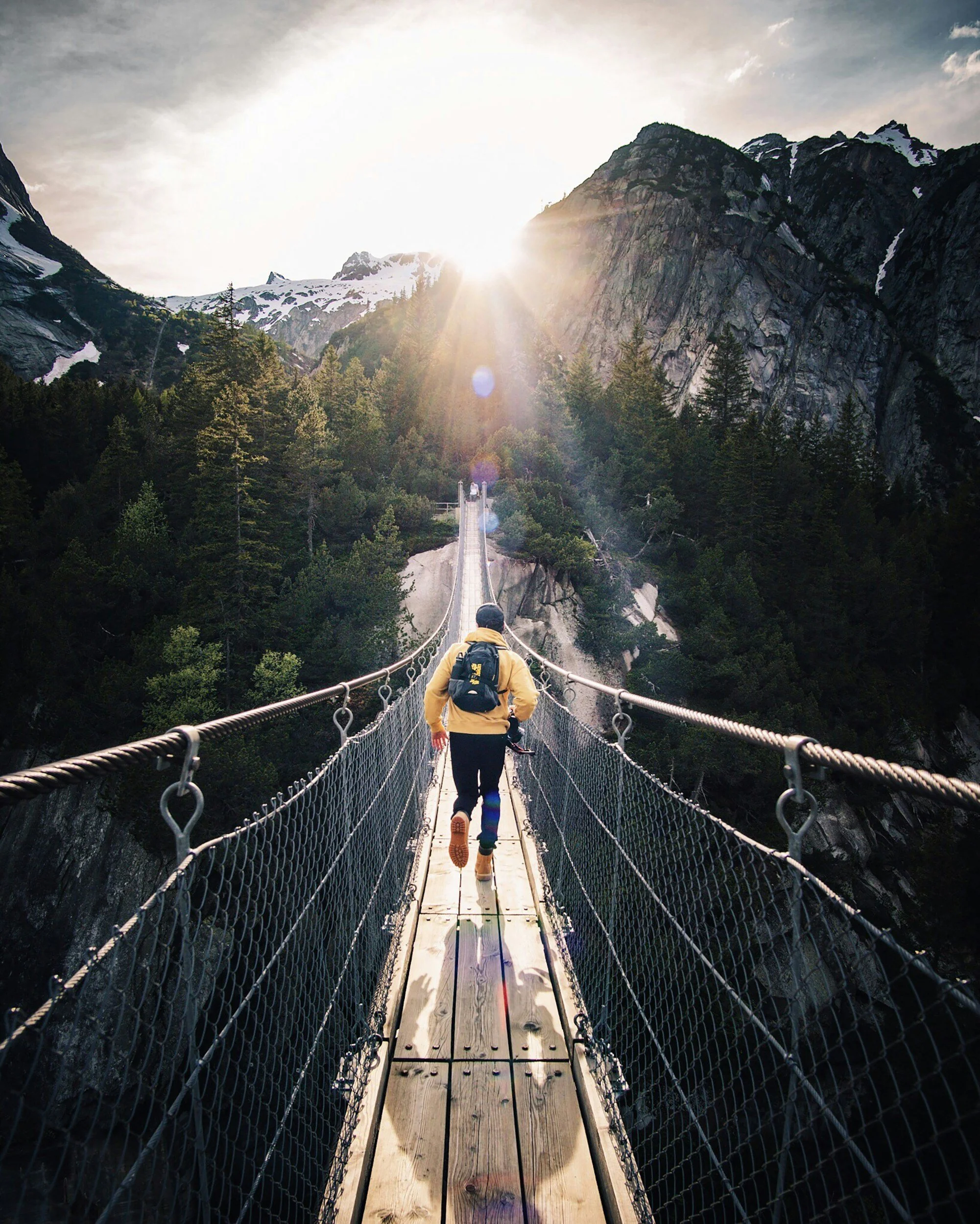 man jogging across a suspension bridge with mountains in the background