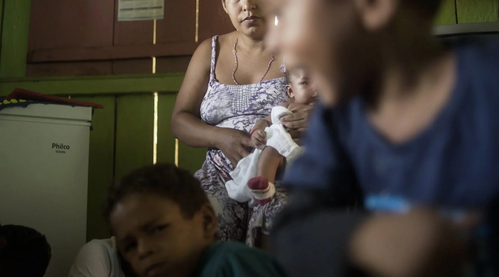 woman holds baby in the background of picture. out-of-focus children play in front of her