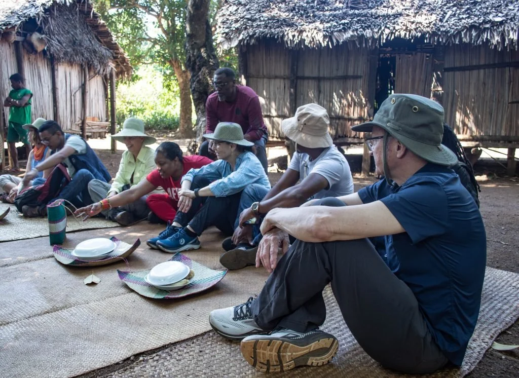 Madagascar team members and HIH donors eat together sitting on woven mats.