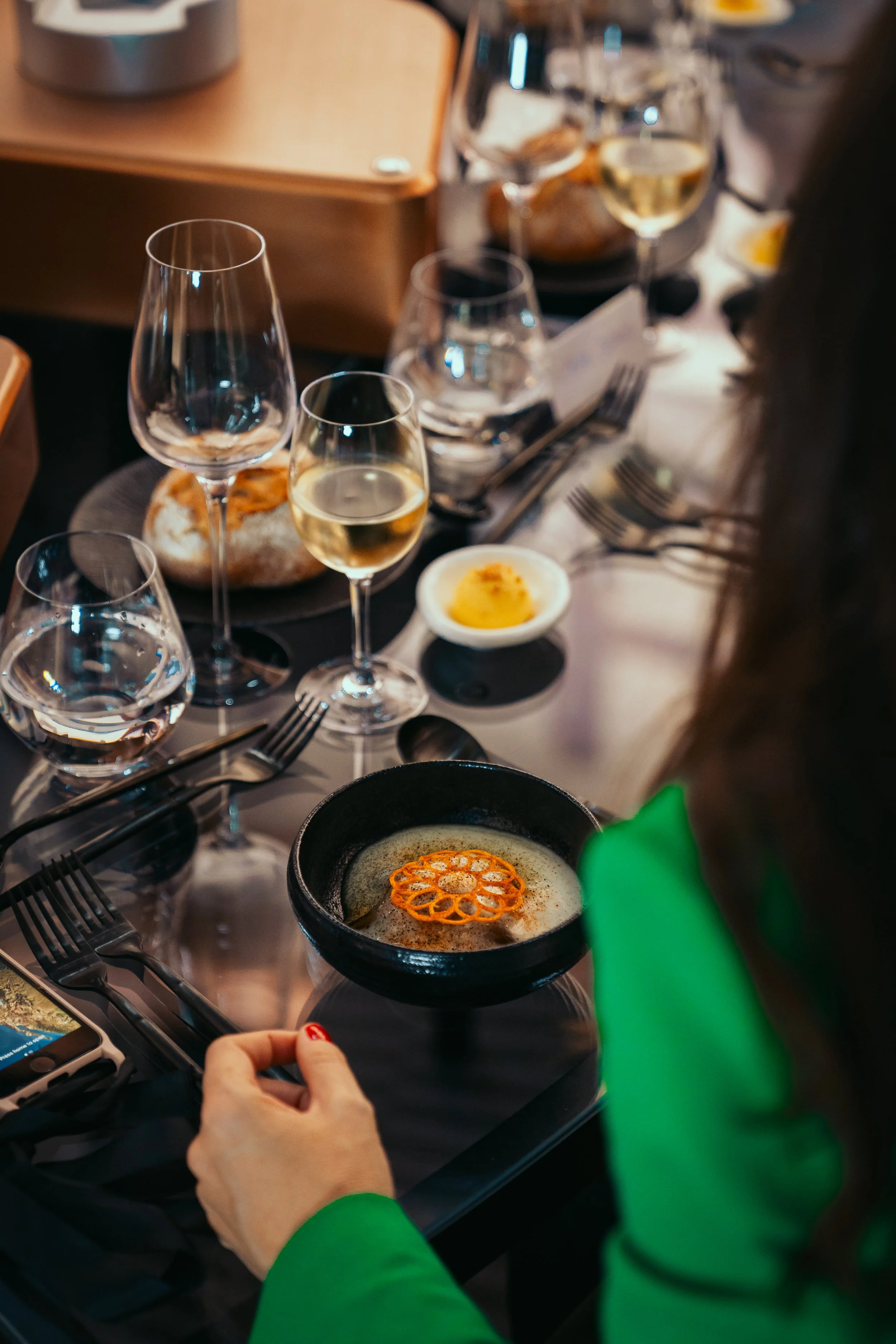 Elegant dinner setting with wine glasses, a plate with bread, and a small dish of sauce on a glass table.
