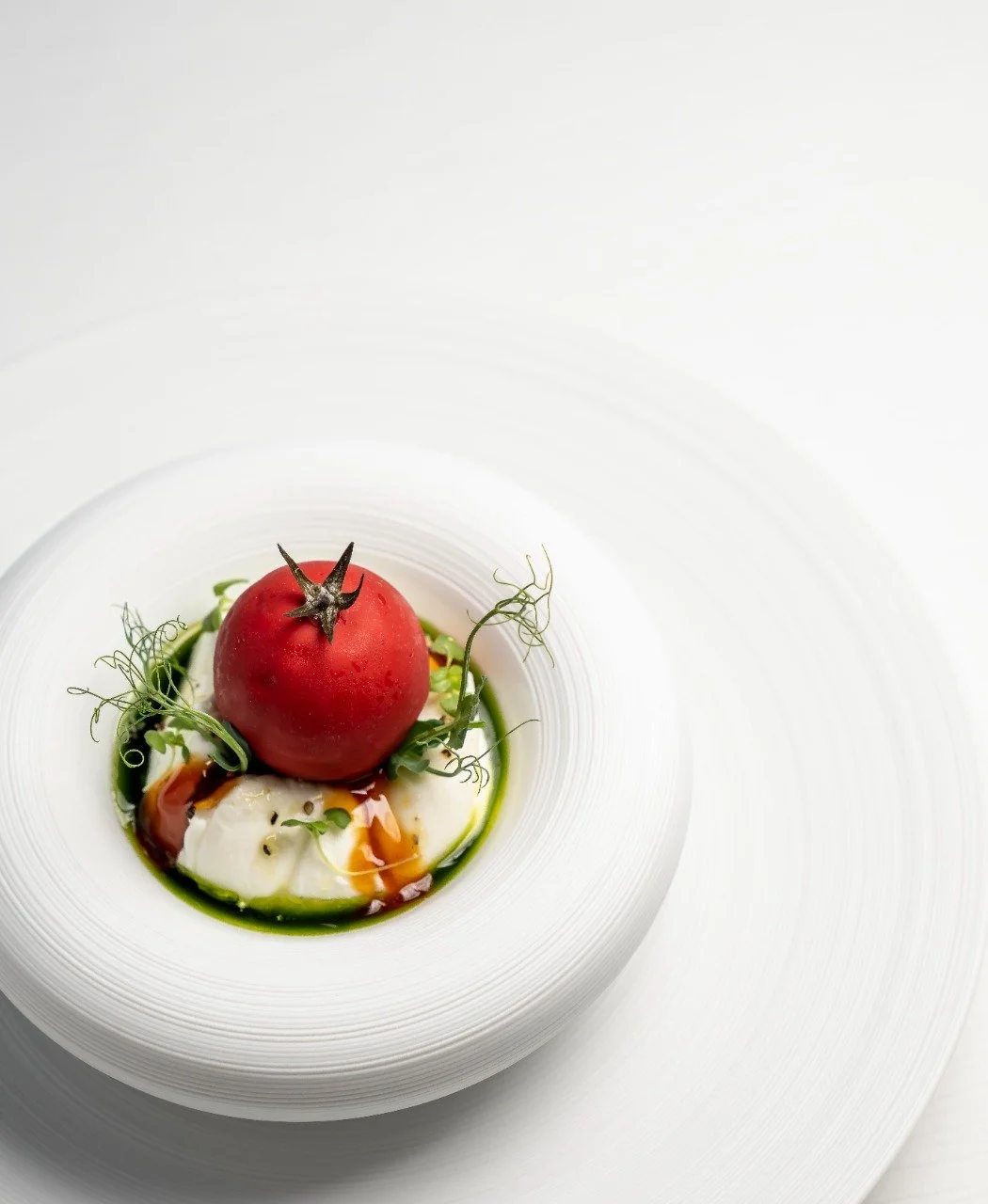 Gourmet dish with a tomato and garnishes on a white plate