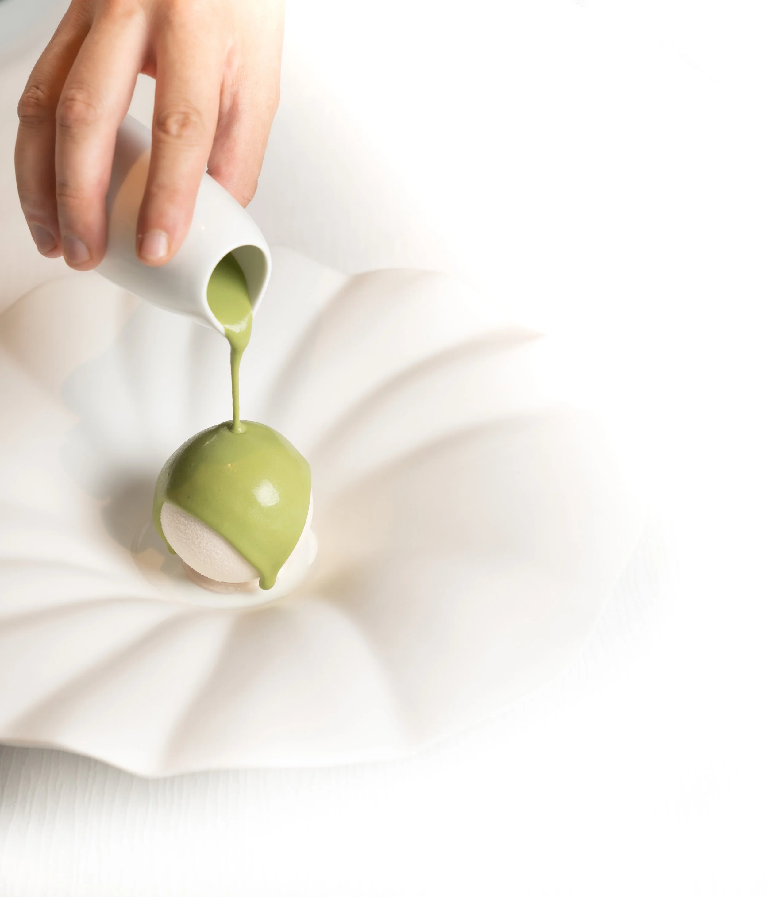 Hand pouring green sauce over a dessert on a white plate.
