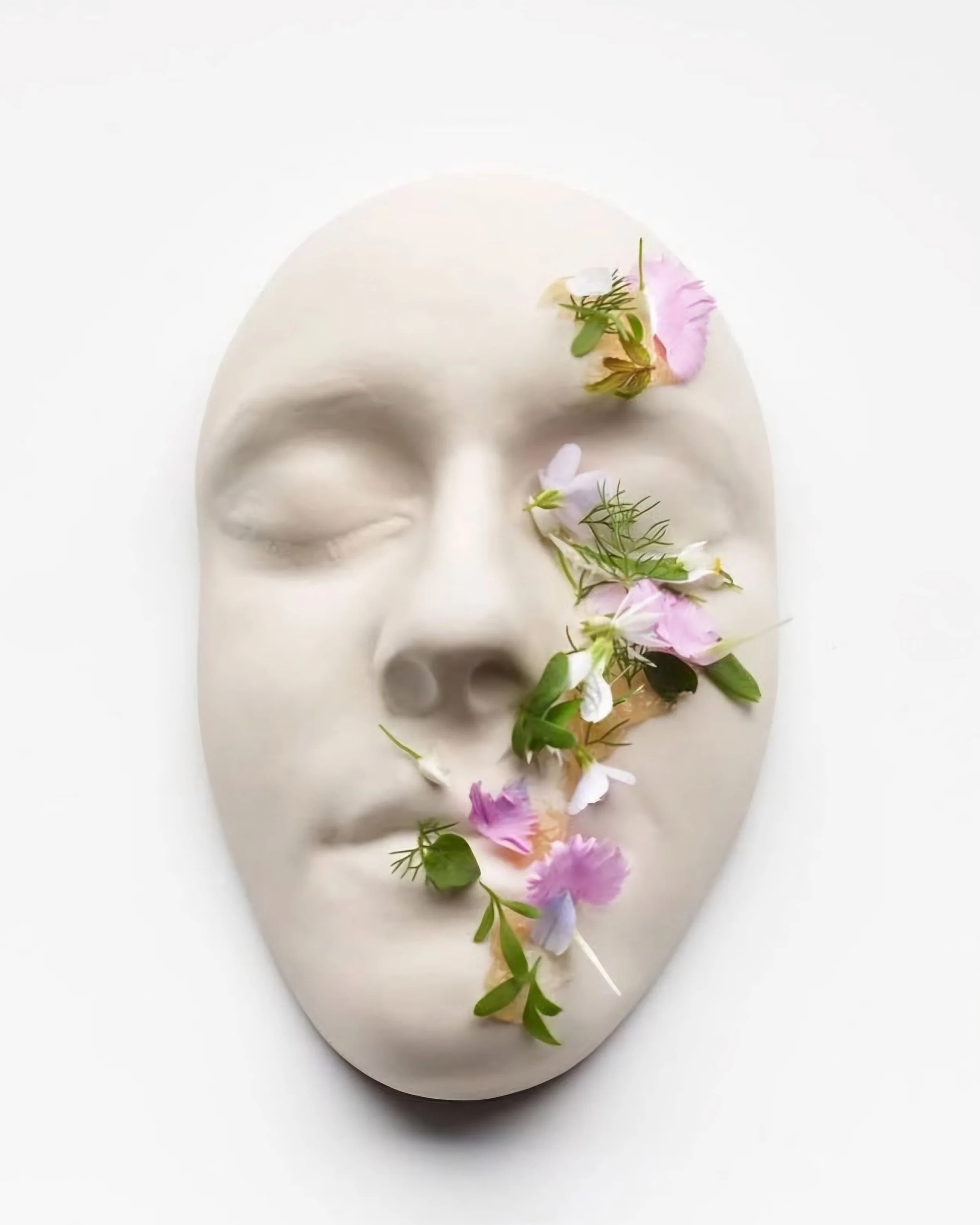 White face mask adorned with colorful flowers and green leaves on a white background.