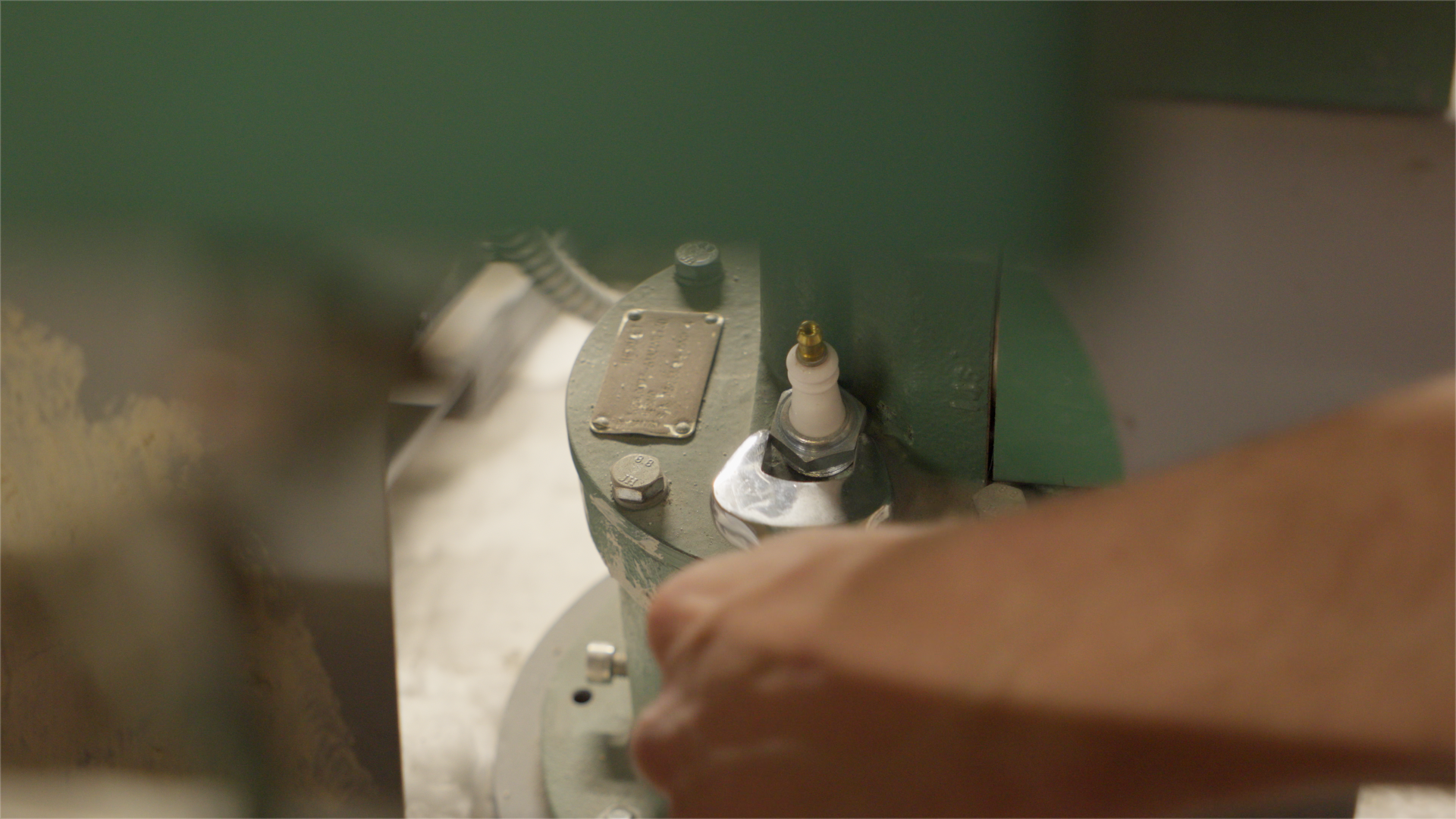 Close-up of industrial machinery with a person's hand working on it, showing metal components and a spark plug.
