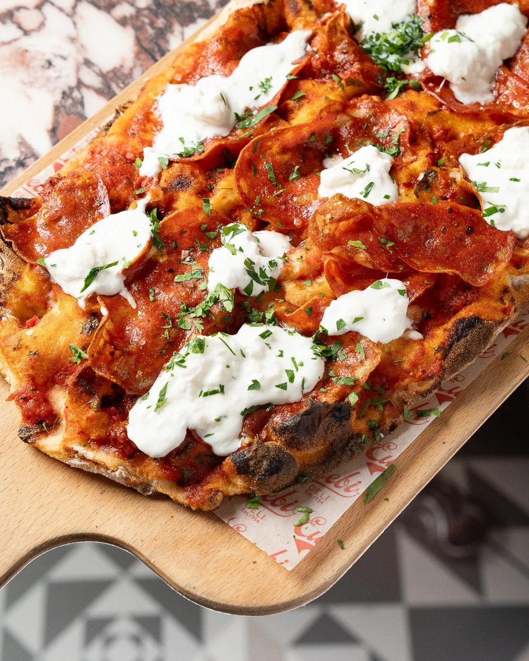Close-up of a rectangular pizza with pepperoni, tomato sauce, melted cheese, ricotta, and parsley on a wooden serving board, taken by a food photographer Glasgow.