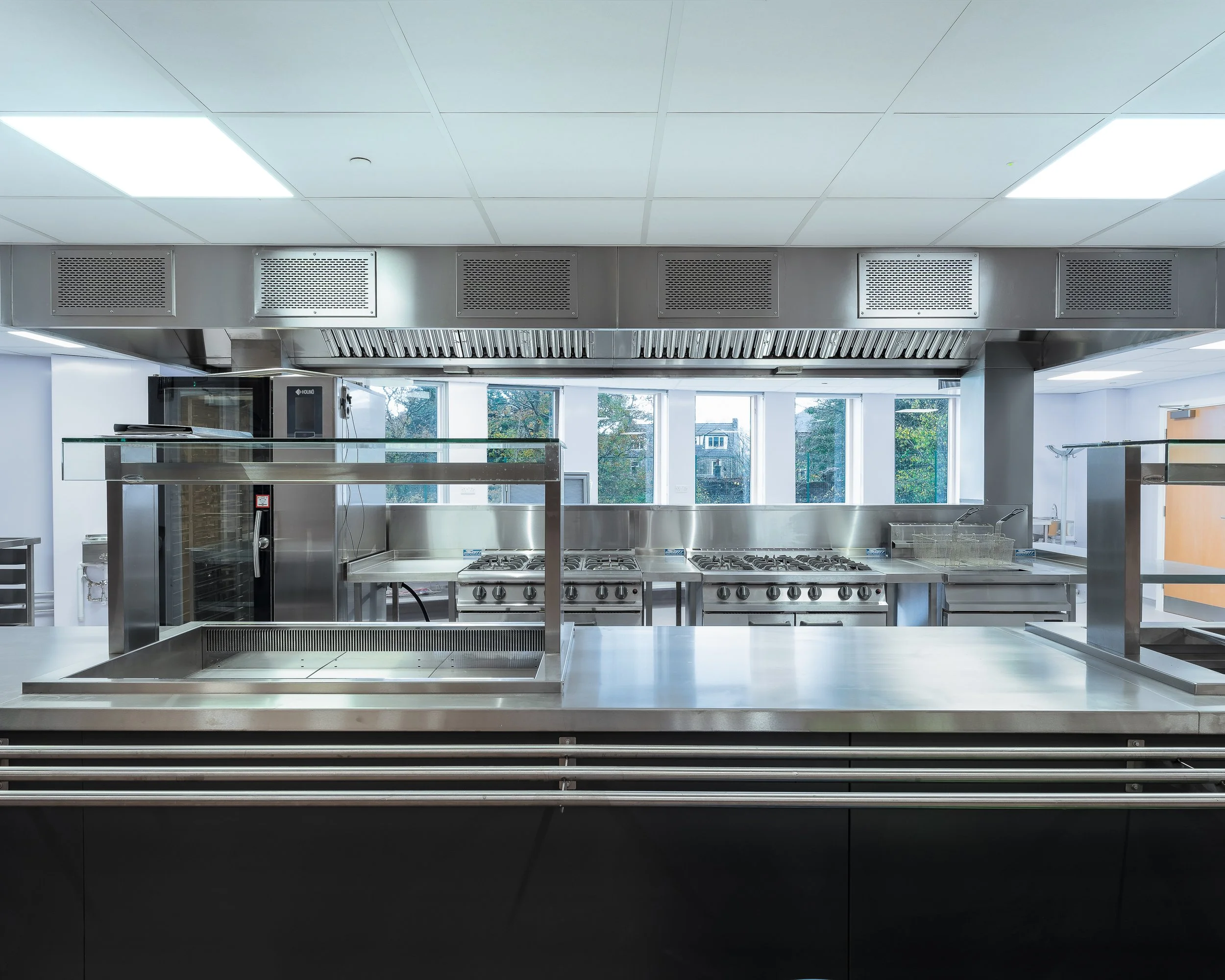 Empty commercial kitchen with stainless steel appliances, stovetops, and a vent hood, taken by a commercial photographer Edinburgh.