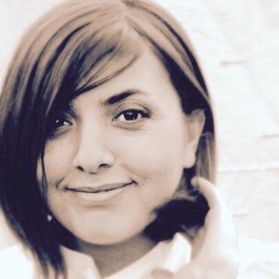 Close-up of a young woman with short dark hair smiling and touching her neck.