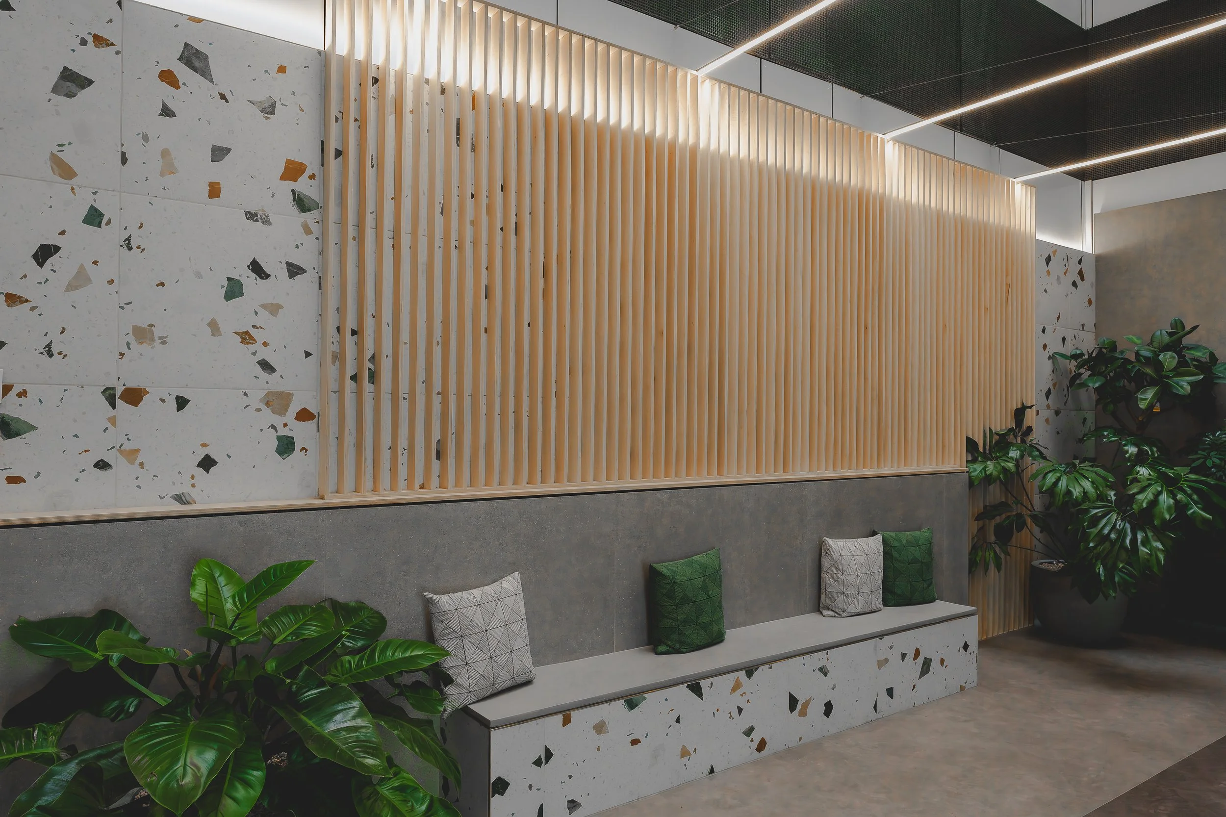 Modern interior with terrazzo wall, wooden slat partition, built-in bench with pillows, and large green plants, taken by an interior photographer Glasgow.