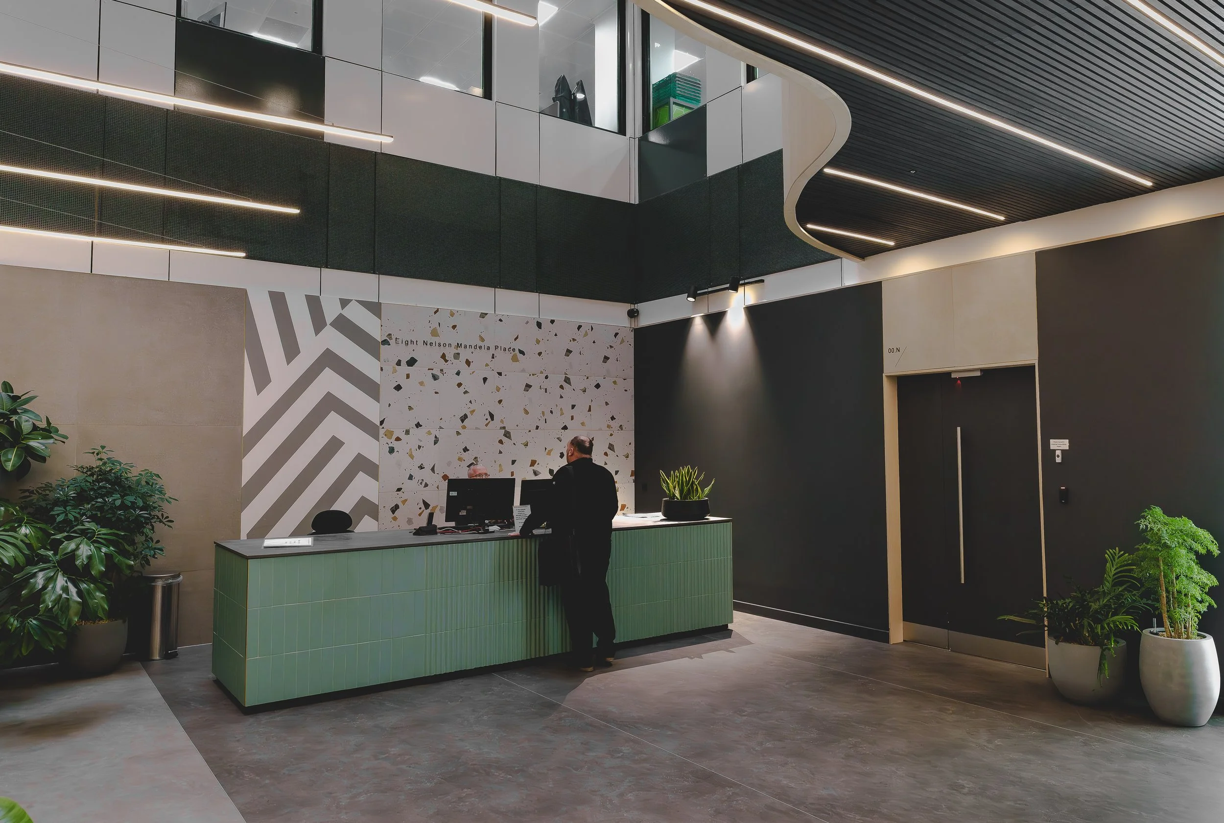 Modern building lobby reception area with two people at the counter, plants, and decorative wall panels, photographed by an interior photographer Edinburgh.