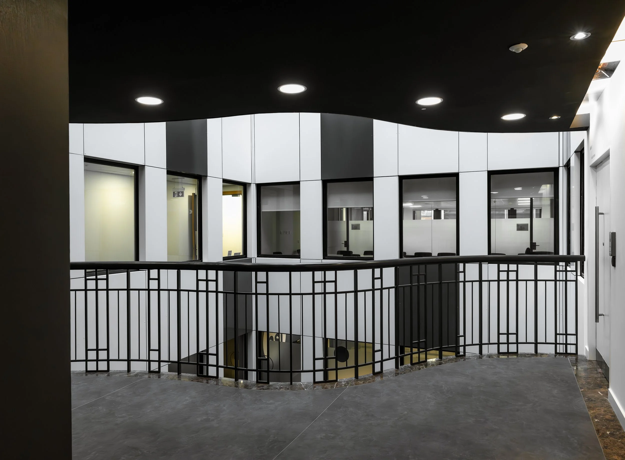 Interior view of a modern office building with black ceiling, white walls, glass windows, and a black metal railing around a staircase, captured by a commercial architectural photographer.