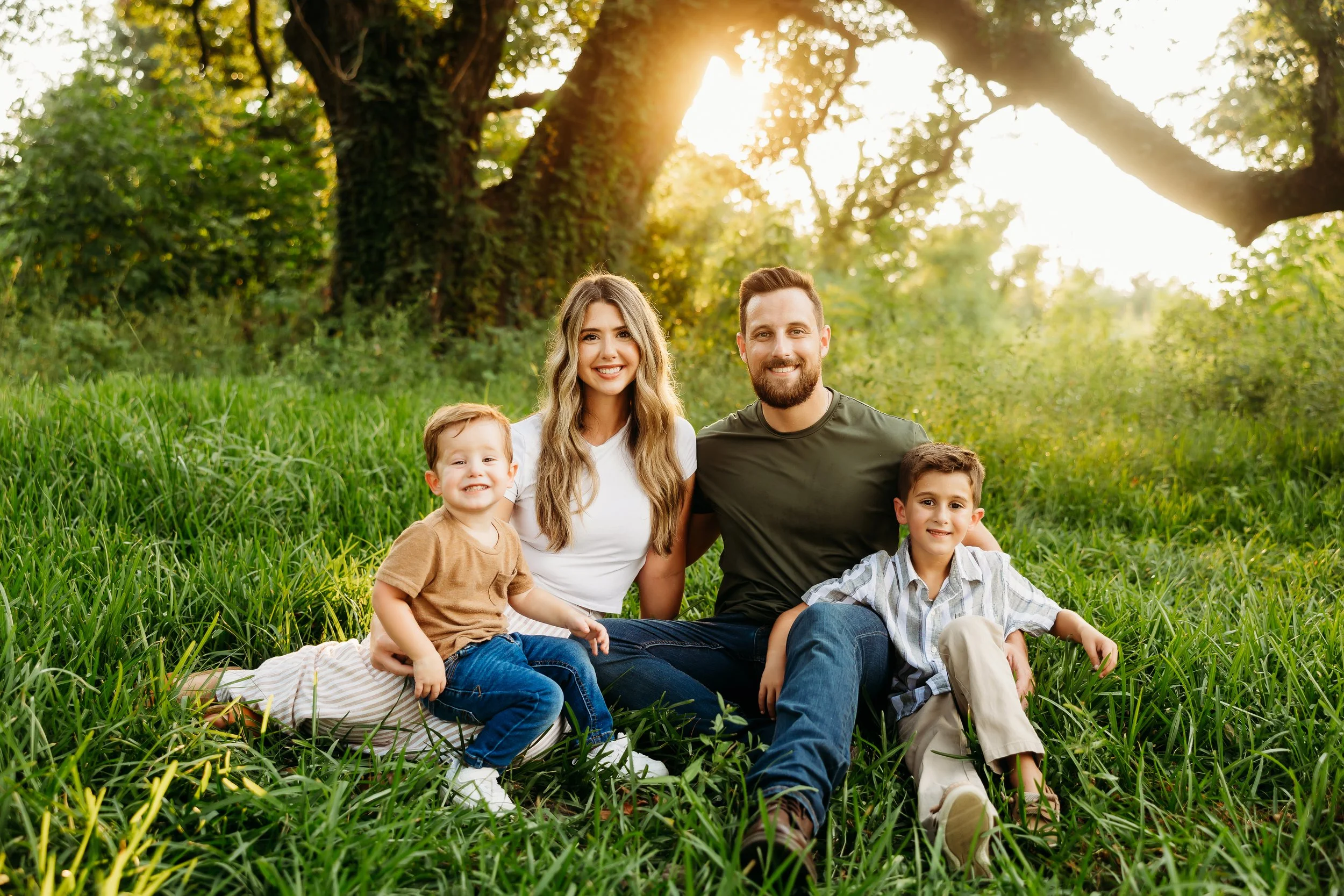 A family sitting on grass in a park with trees in the background, enjoying the sunlight.