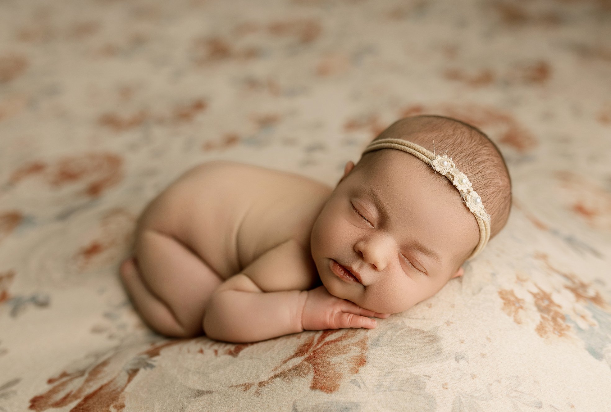 A baby wrapped in a mustard yellow blanket, positioned against a matching yellow background, with wide eyes looking directly at the camera.