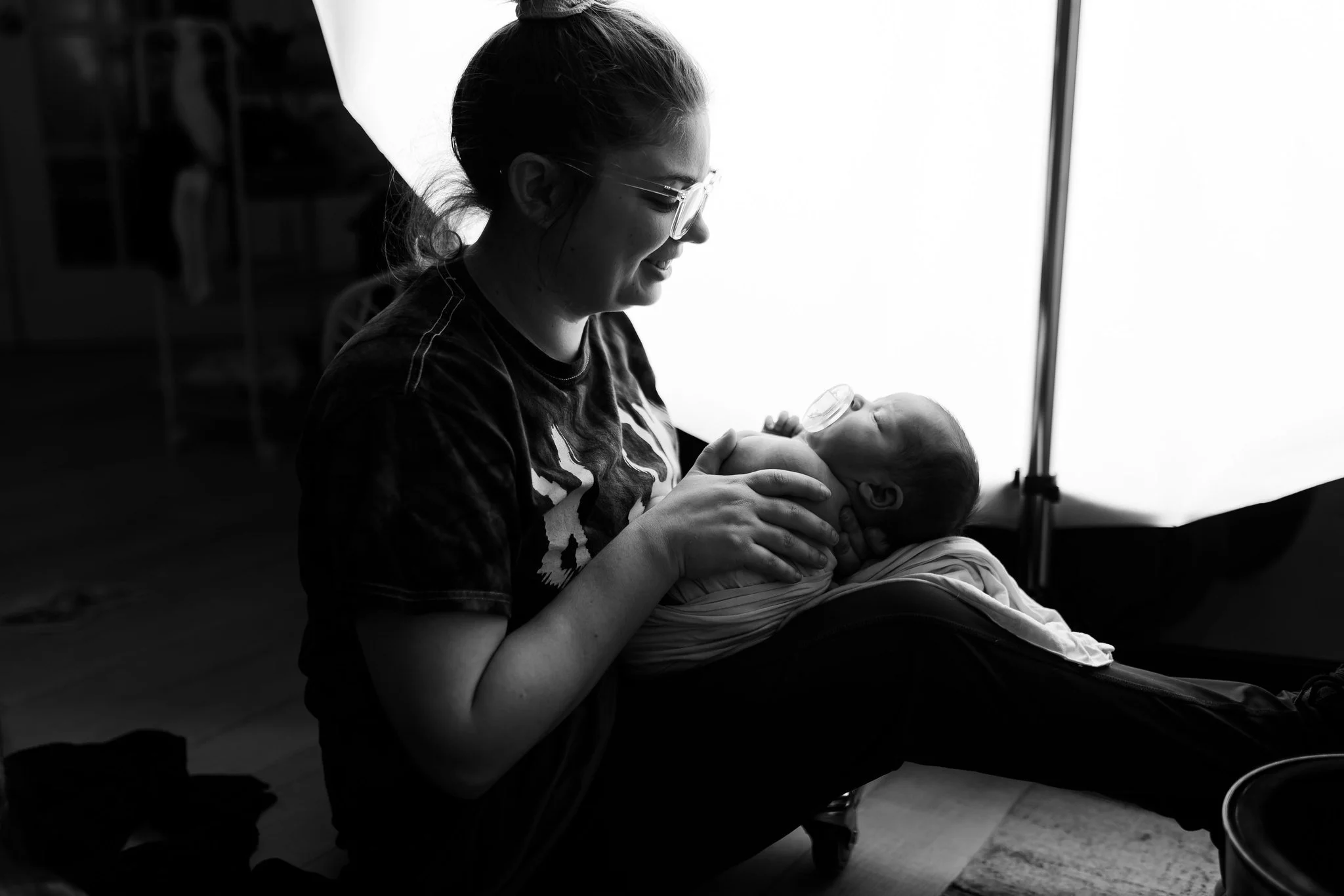A woman with glasses holding a newborn baby in her arms, both sitting indoors.