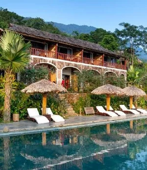 A luxury resort pool surrounded by thatched villas and palms
