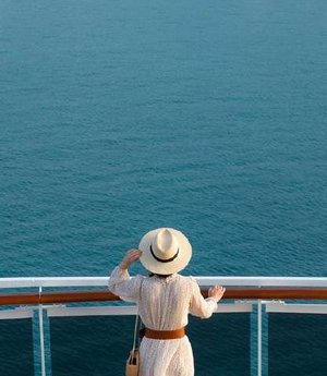 A traveller in a sun hat looking out from the deck of a cruise ship