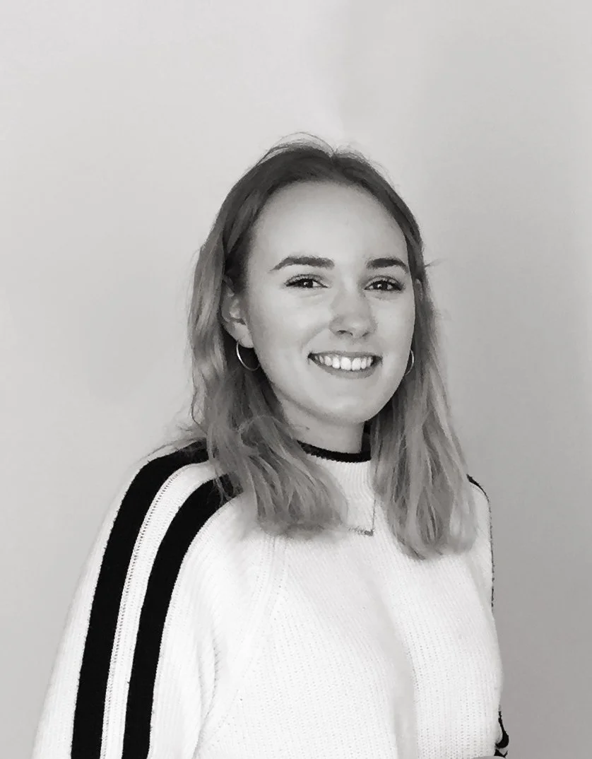 Black and white photo of a woman smiling, wearing a white sweater with black stripes on the sleeves.