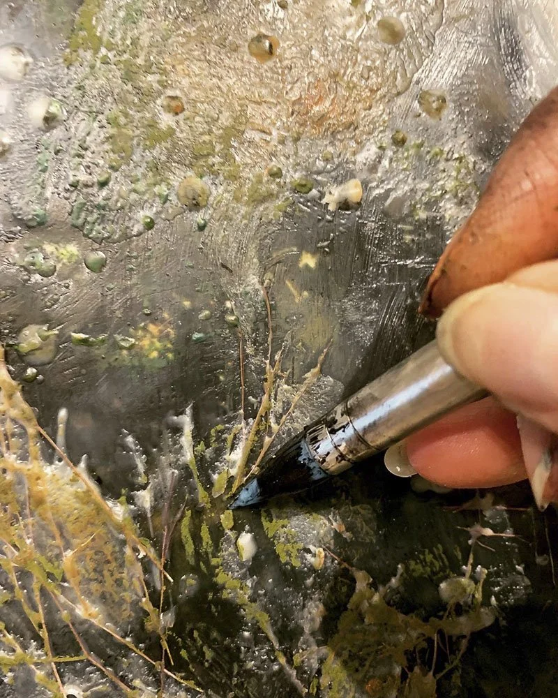 Close-up of a person paining using encaustic medium, creating texture in the wax on a wooden surface.