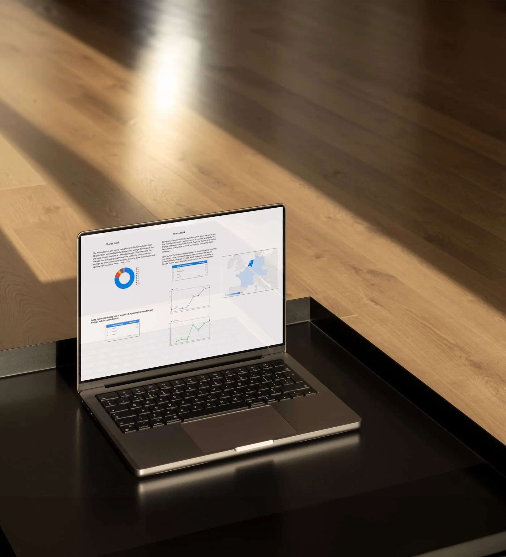 A laptop on a black table displaying graphs and charts, with sunlight casting shadows on a wooden floor.