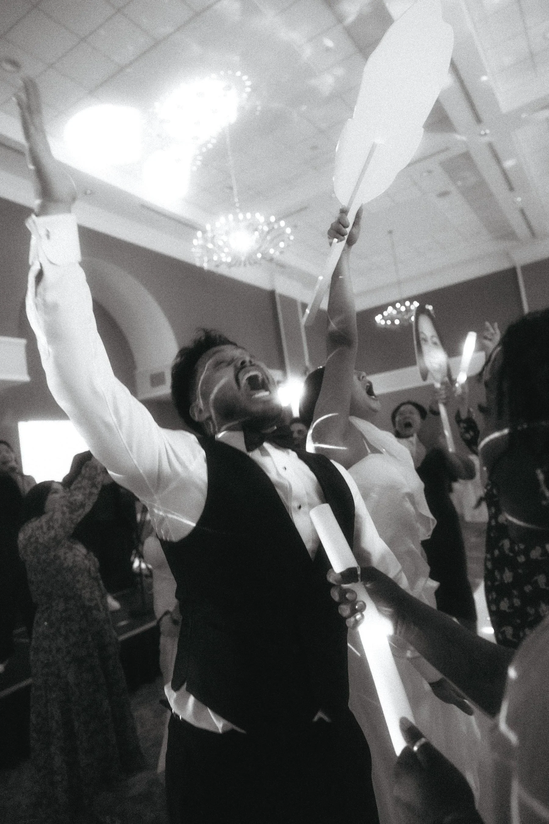 People celebrating at a party, holding up paper fans and smiling joyfully, in a decorated indoor venue.