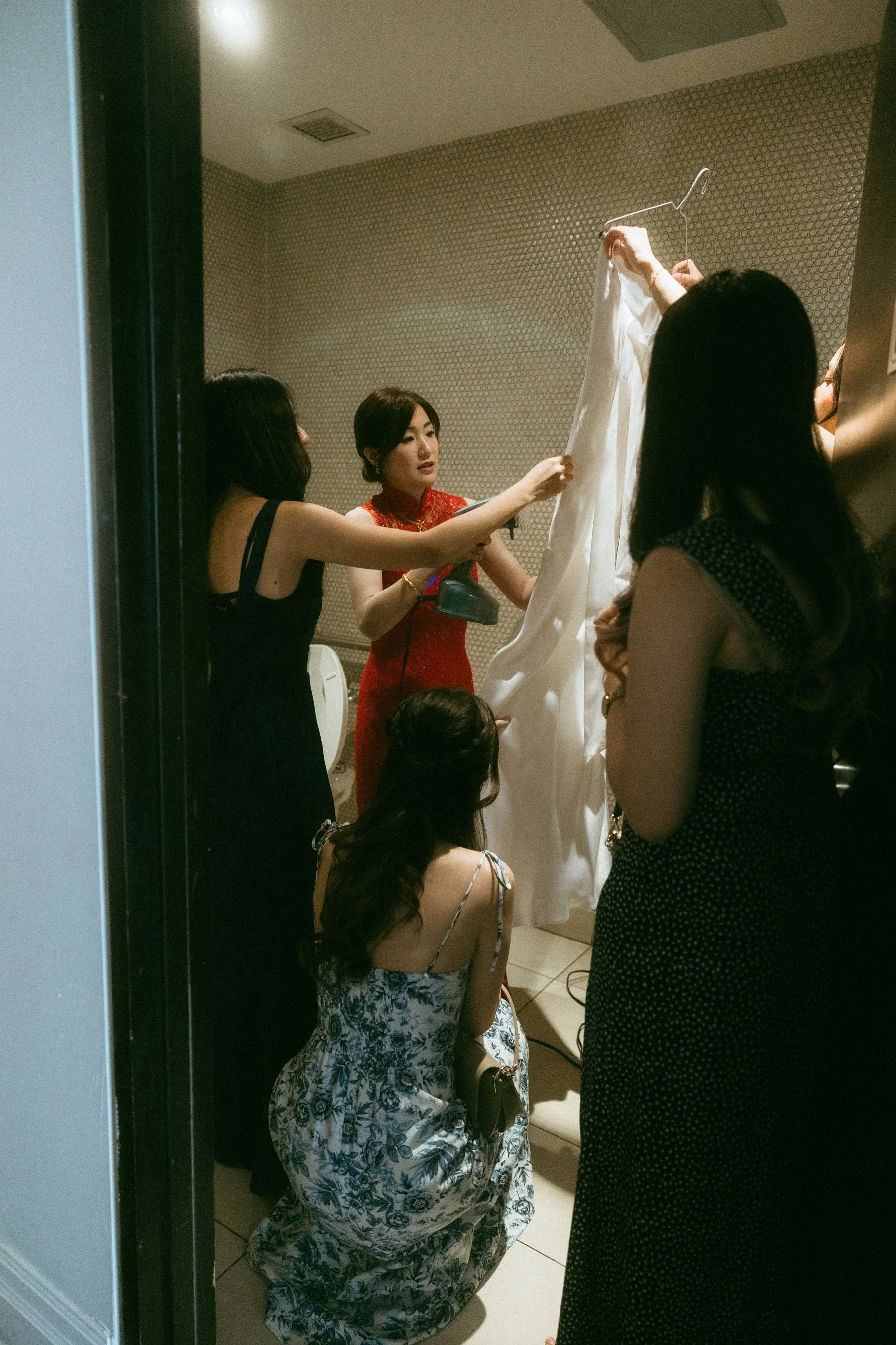 Group of women examining a white dress on a hanger in a fitting room.