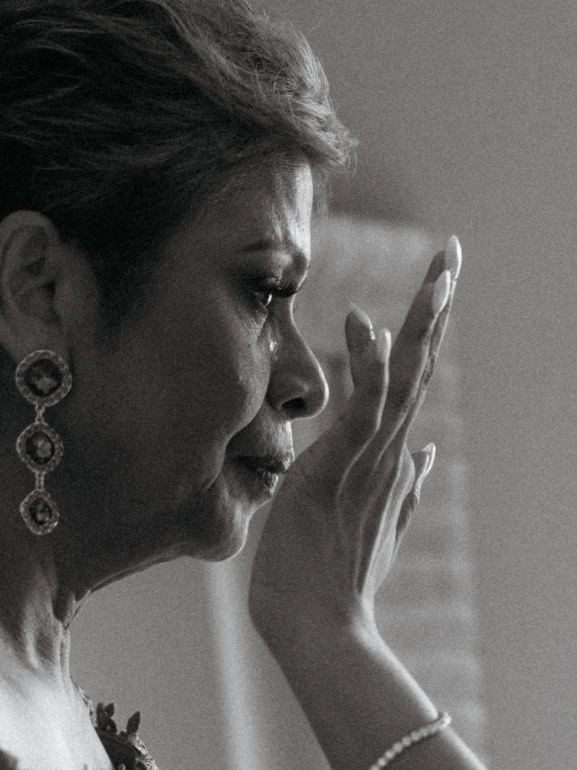 A black and white photo of a woman with her eyes sad and her hand on her forehead, wearing earrings and a necklace.