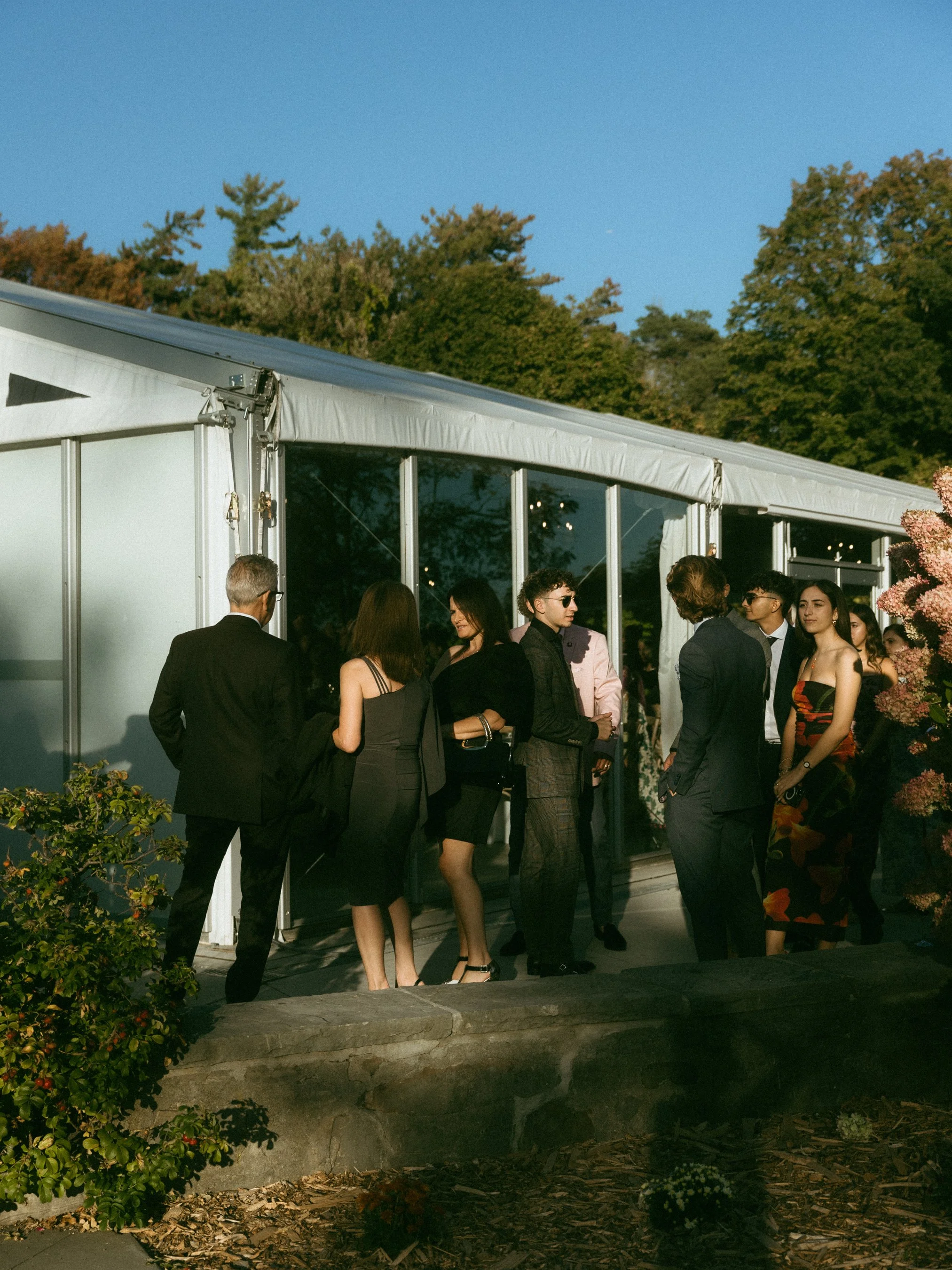 Group of people engaged in conversation outside a large white event tent during sunset.