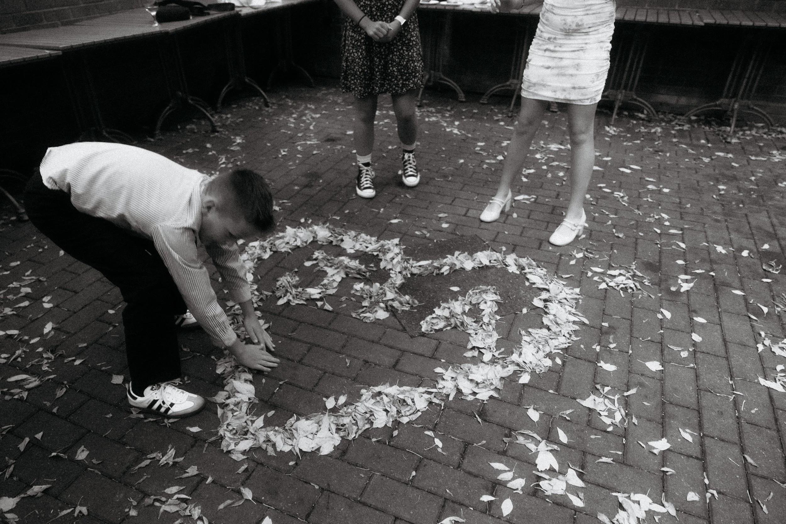 Children drawing with leaves on a brick sidewalk, surrounded by fallen leaves.