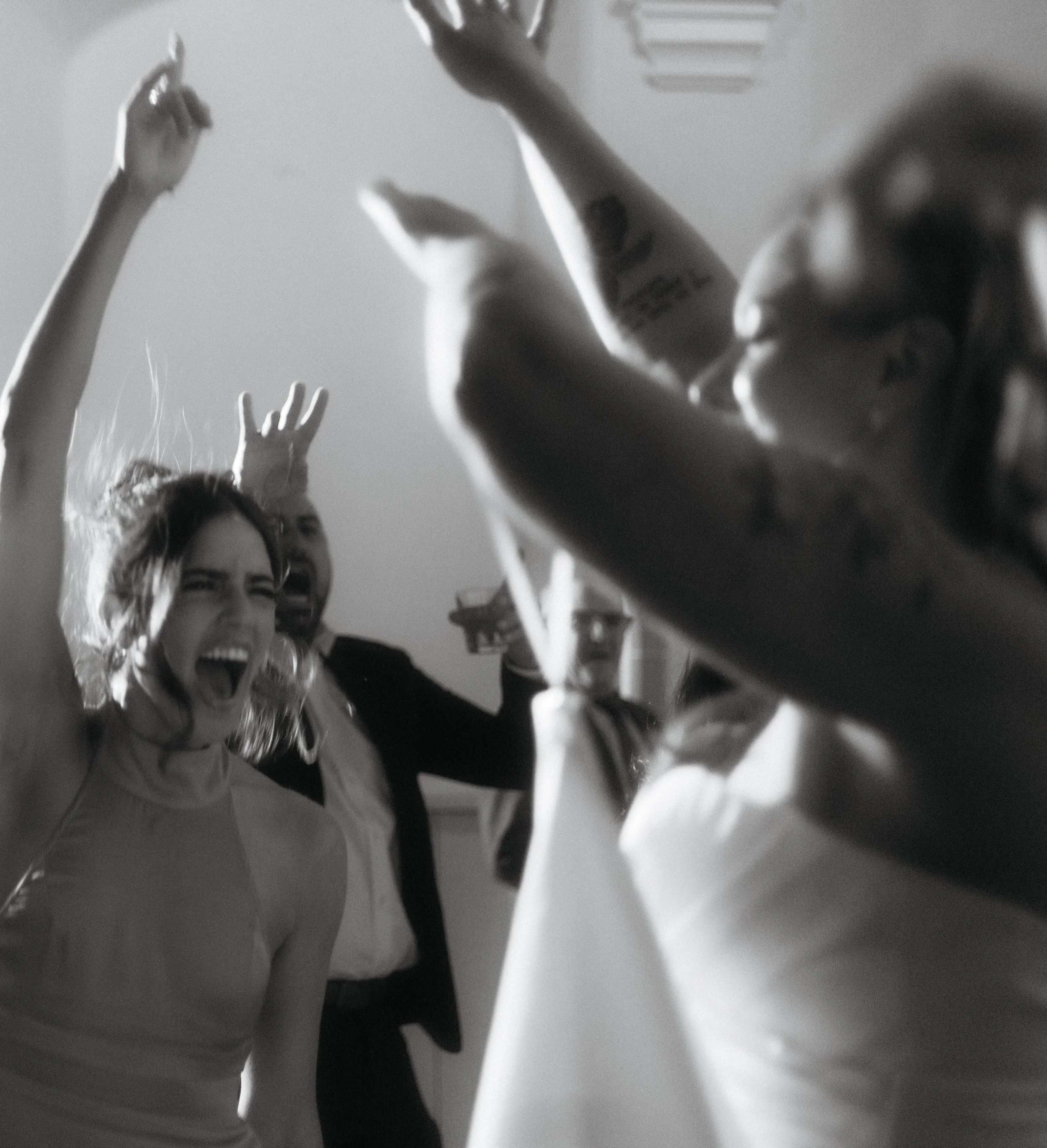 Group of people dancing and celebrating indoors, some with arms raised, smiling and laughing.