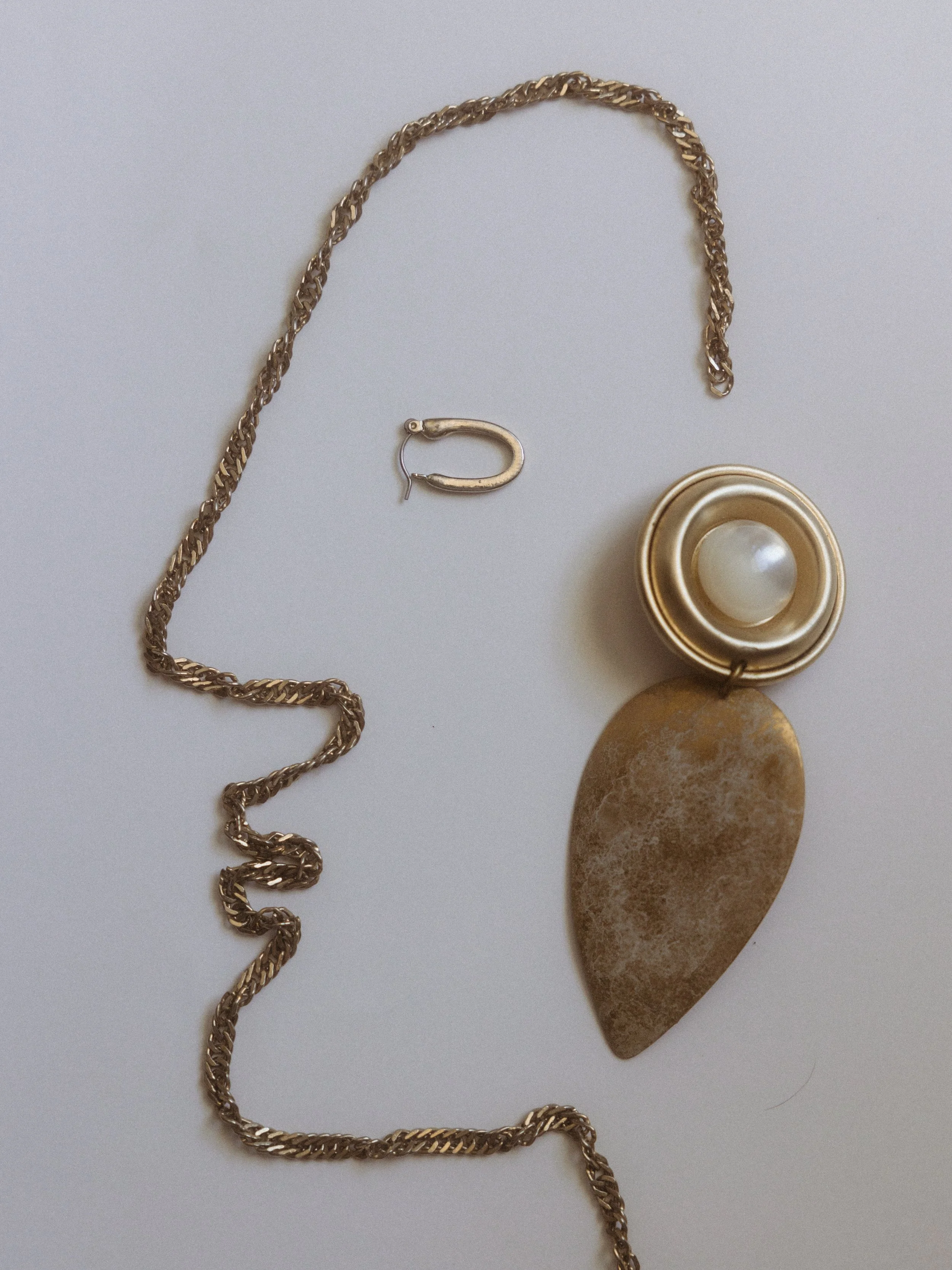 Gold jewelry including a chain necklace, a hoop earring, and a brooch with a pearl and leaf-shaped pendant on a white background.