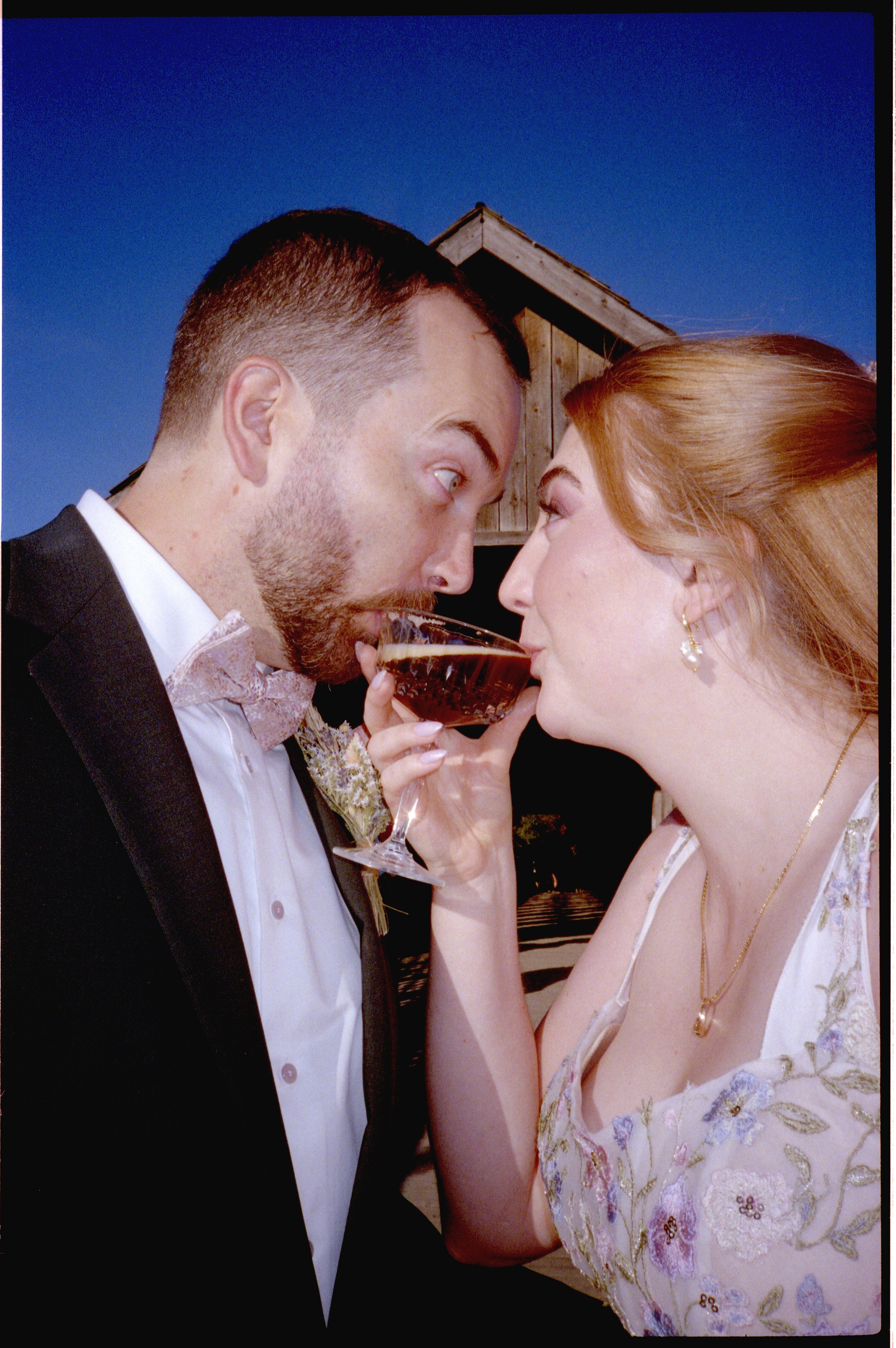 A couple in formal attire sharing a drink outdoors at night, with a barn visible in the background.