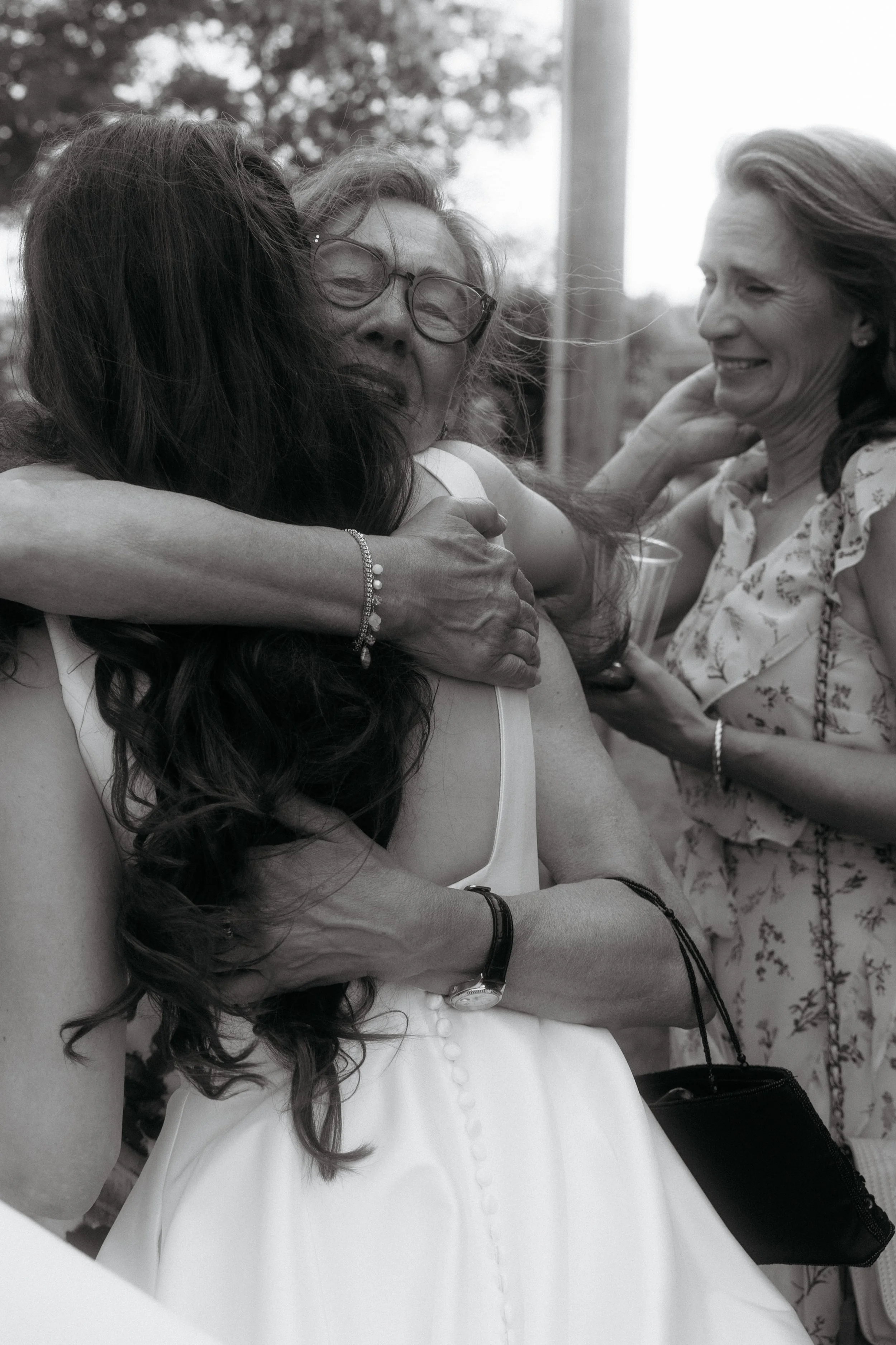 Group of women hugging each other at an outdoor gathering, emotional moment, black and white photo.