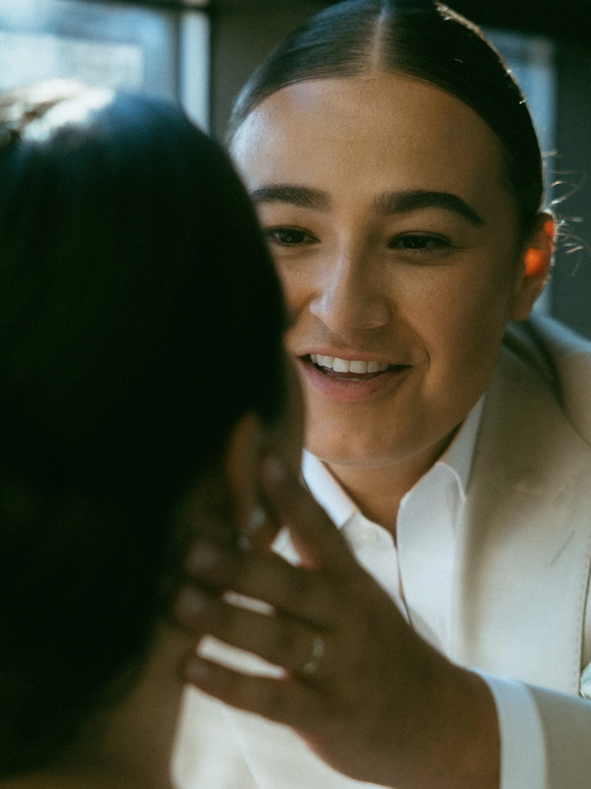 Close-up of two women engaged in a conversation, one facing the camera with a smile, and the other's profile visible, with natural lighting and a blurred background.