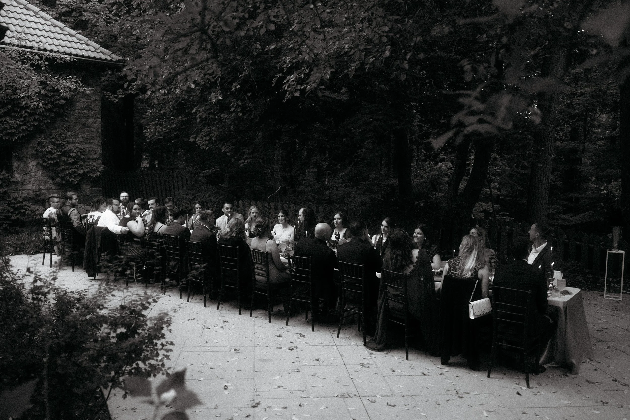 A large outdoor dinner gathering with many people seated at a long table in a wooded area at night.