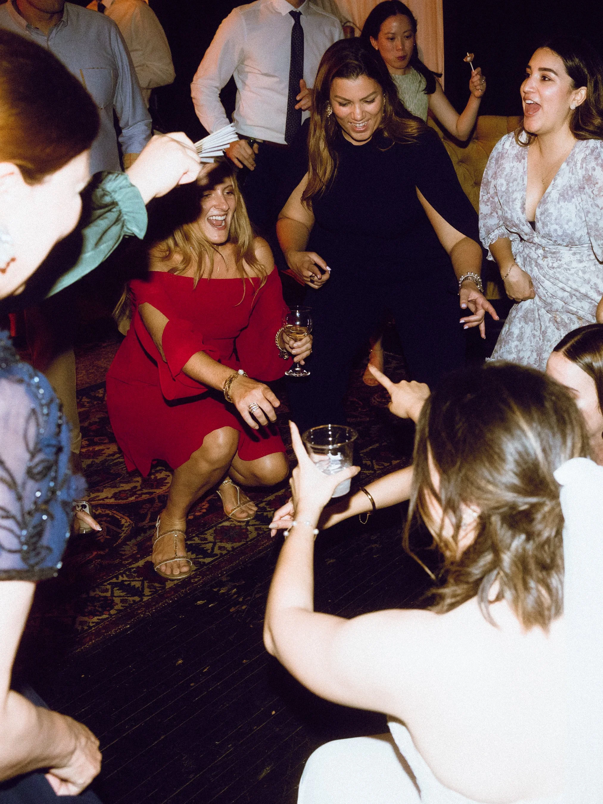 People dancing and having fun at a social gathering or party, with women laughing and holding drinks.