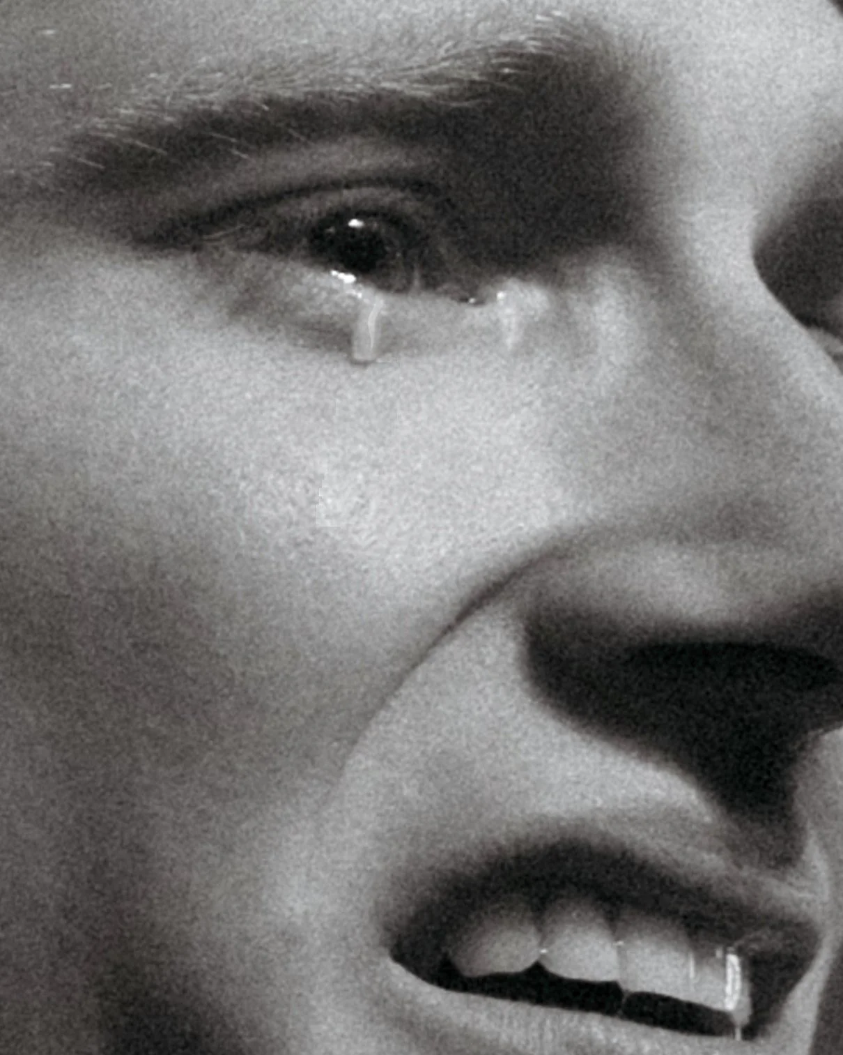 Close-up of a child's face in black and white, showing a tear rolling down their cheek and an expression of sadness or distress.