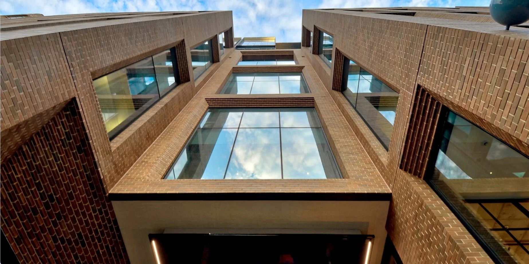 Low-angle view of a Barrack Place with large glass windows, reflecting the partly cloudy sky, taken from ground level looking upward.