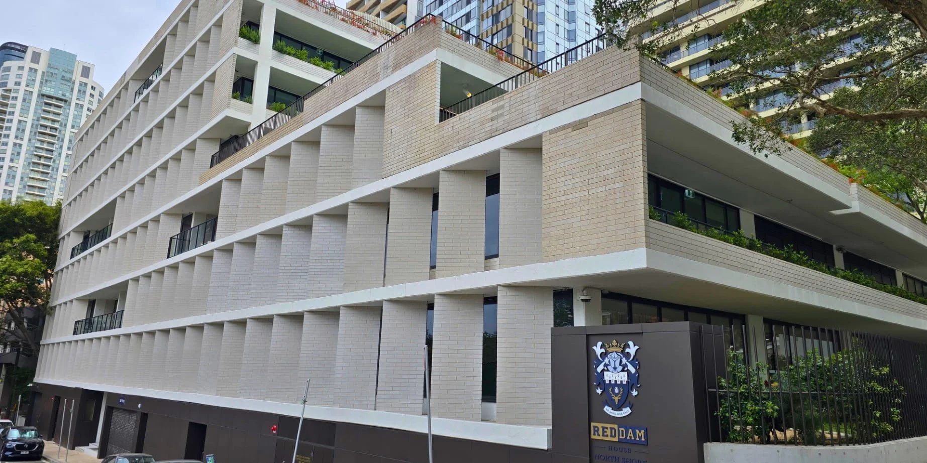 Side angle view of 41 McLaren st showcasing white brickwork. Skyscrapers are in the background of the shot with trees.