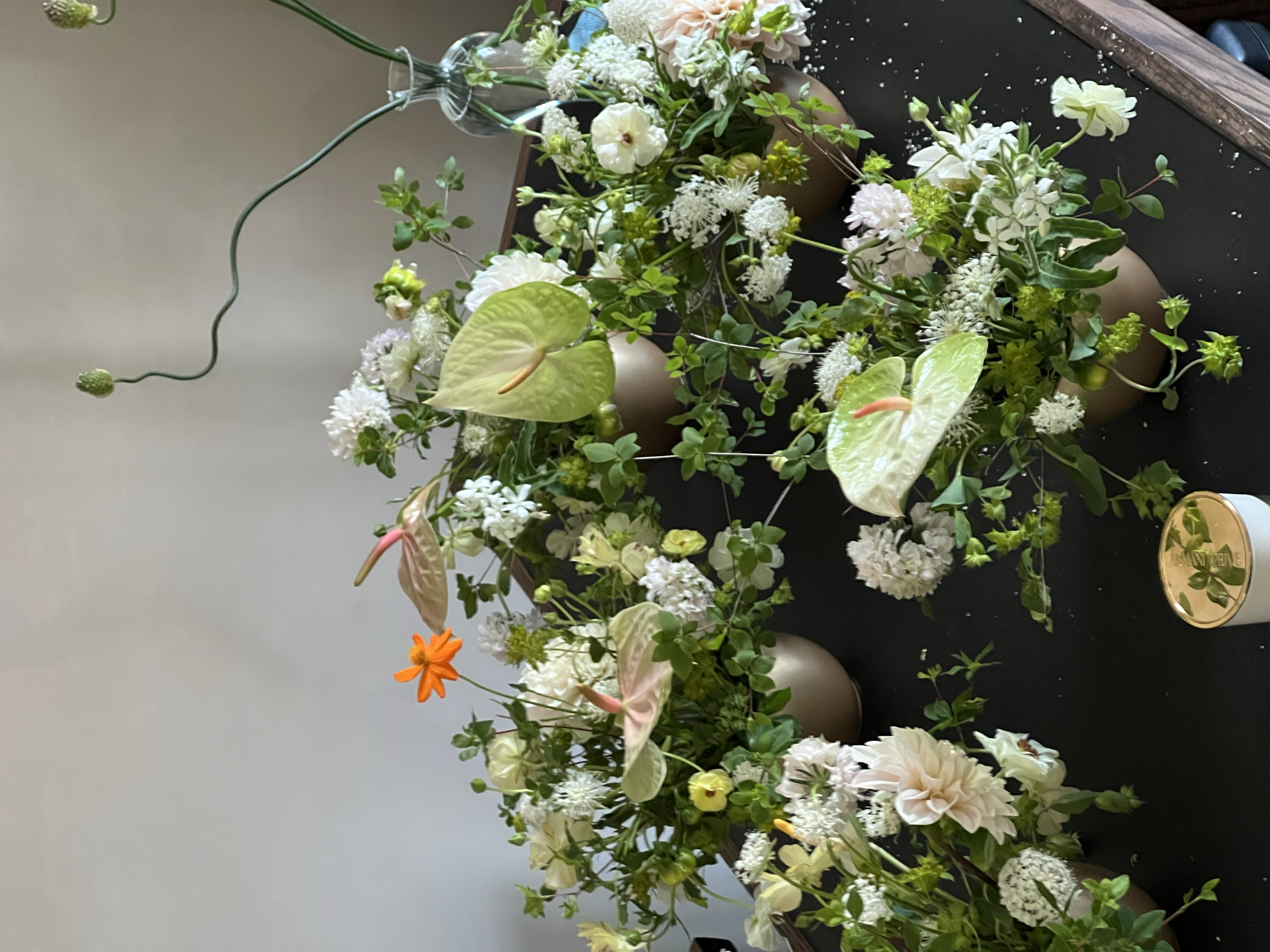 A floral arrangement with various white and cream-colored flowers including anthuriums, anemones, and other blossoms, displayed in vases on a black surface.