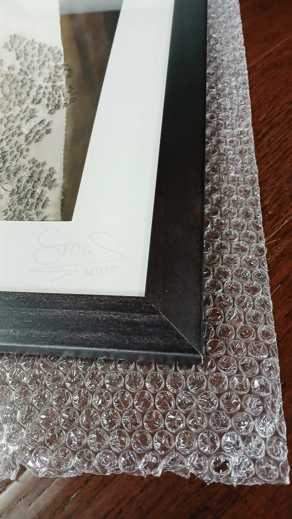 Framed ink drawing titled "The Lighthouse" by New Zealand artist Sina Sibler, featuring a Fiordland crested penguin and fur seal illuminated by a lighthouse beam.