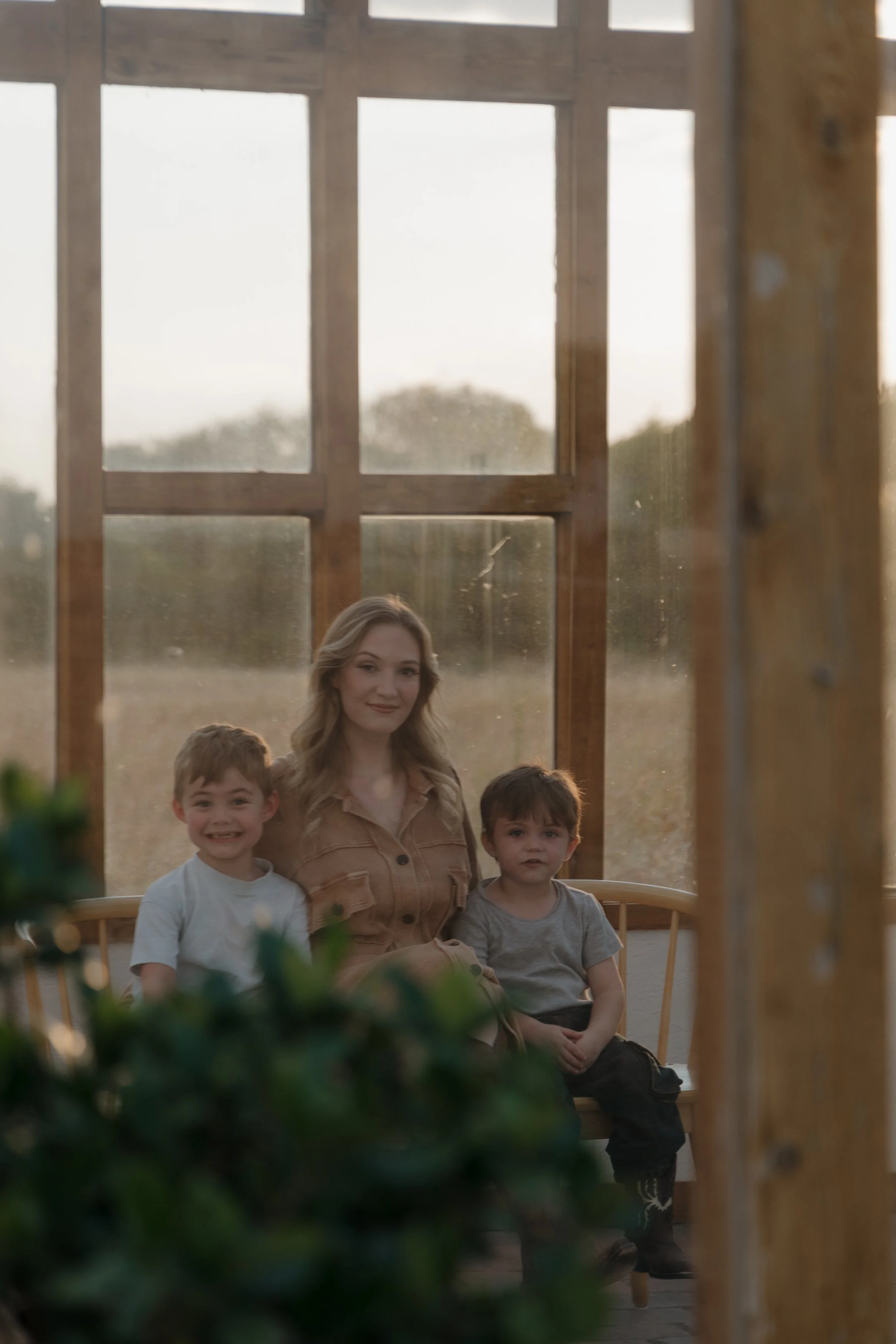 A woman with three children sitting outside near a wooden structure during sunset, with trees and sky in the background.