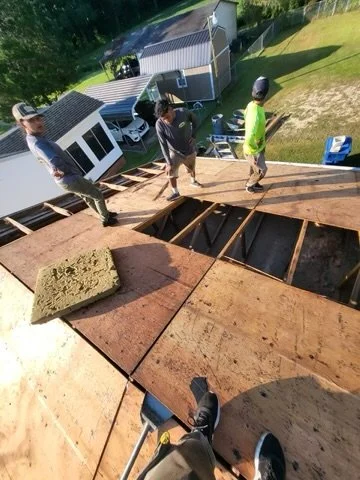 Three people walking on a rooftop under construction with building materials and tools visible.