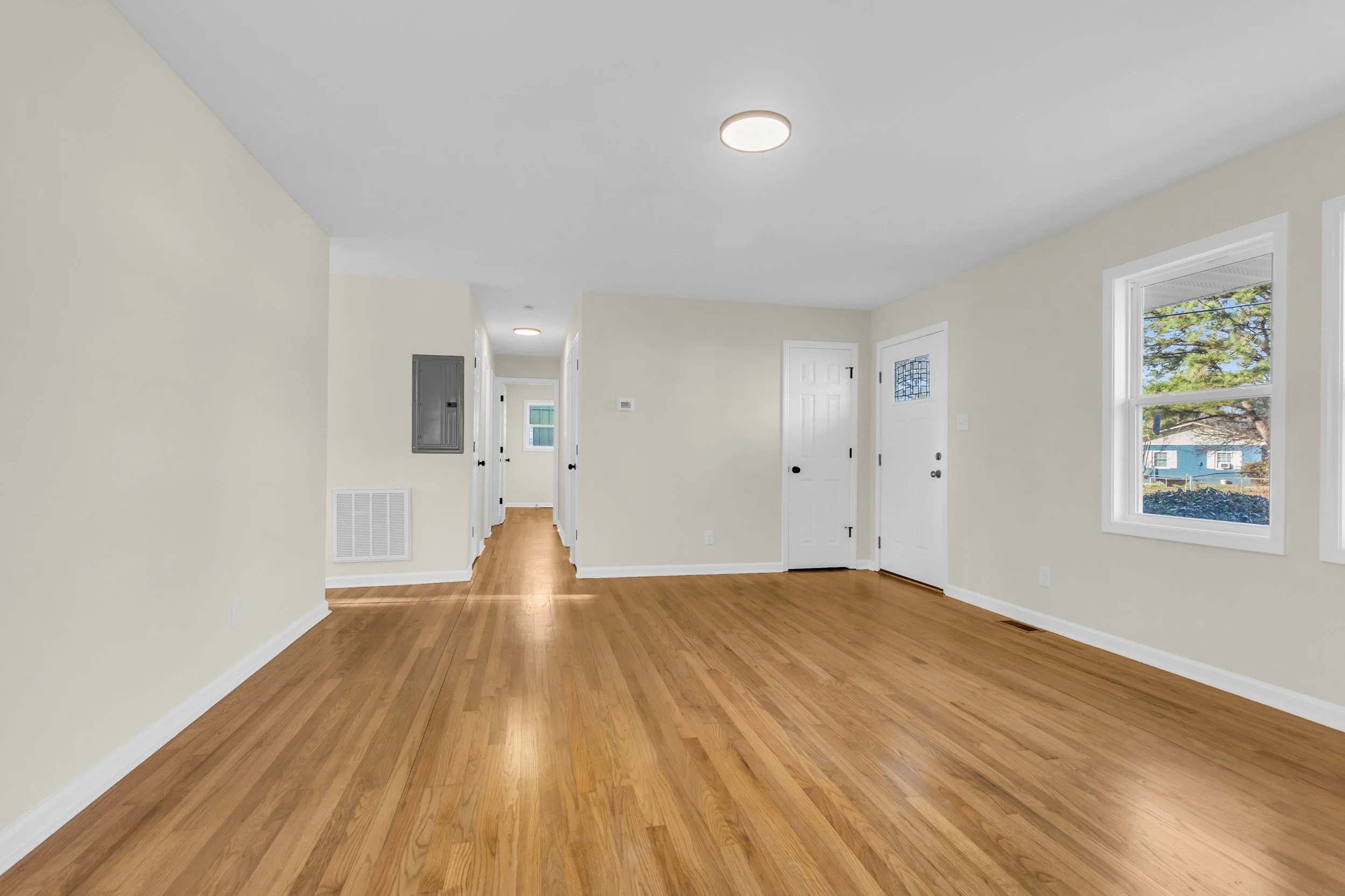 Empty living room with hardwood floors, cream walls, two large windows, white trim, and ceiling lights.