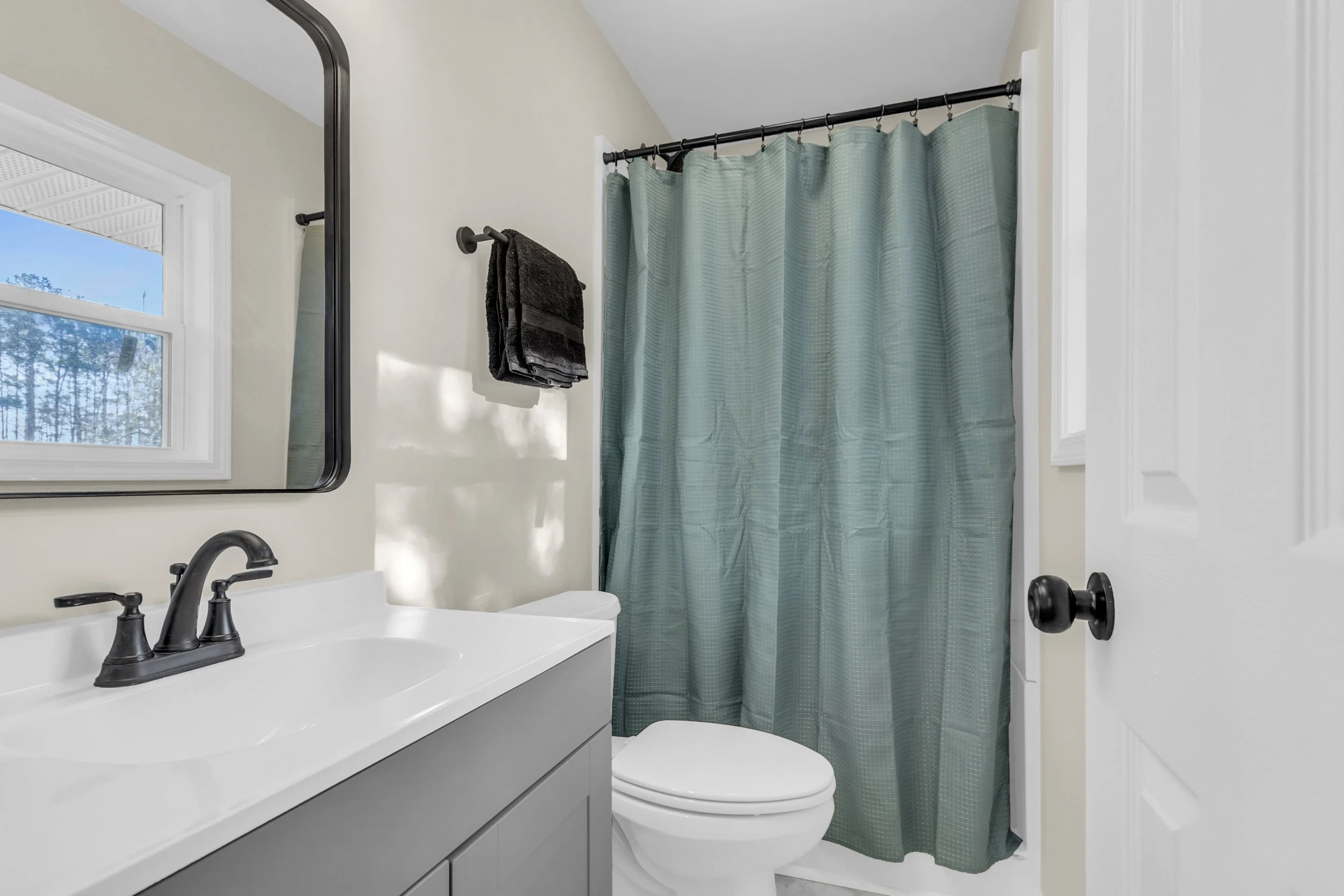 Bathroom with a white sink, black faucet, a mirror, a window, a towel on a black towel rod, and a shower with a teal curtain.