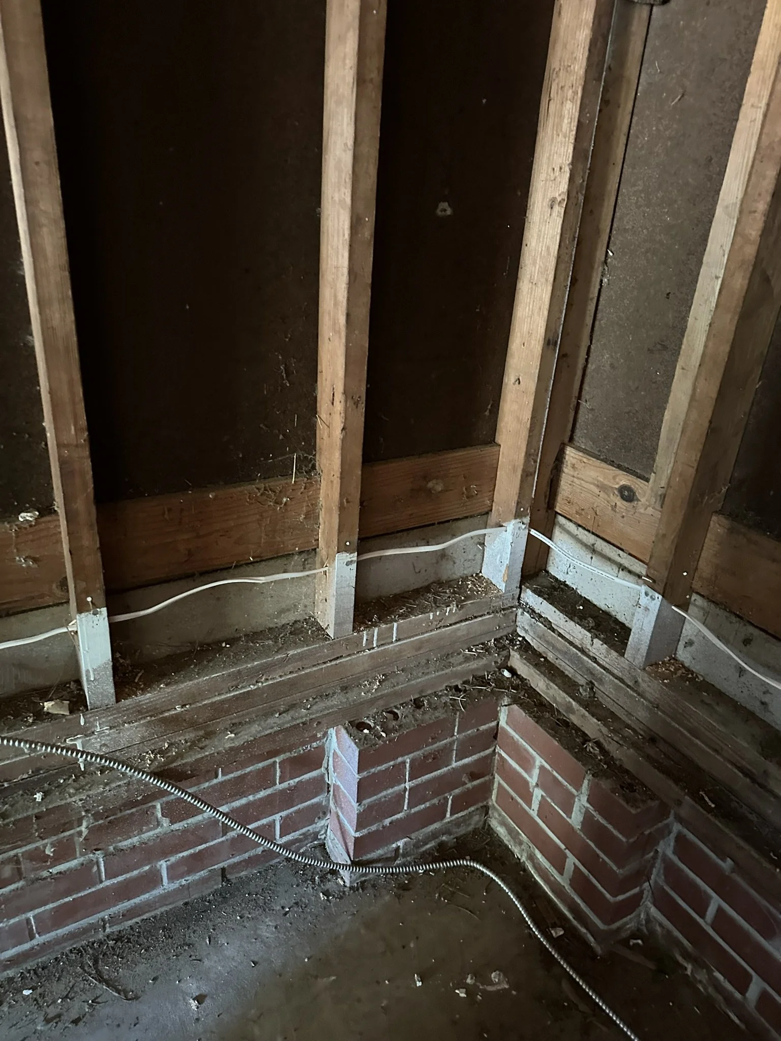 Interior section of a building under renovation showing exposed wooden studs, brick foundation, and electrical wiring.