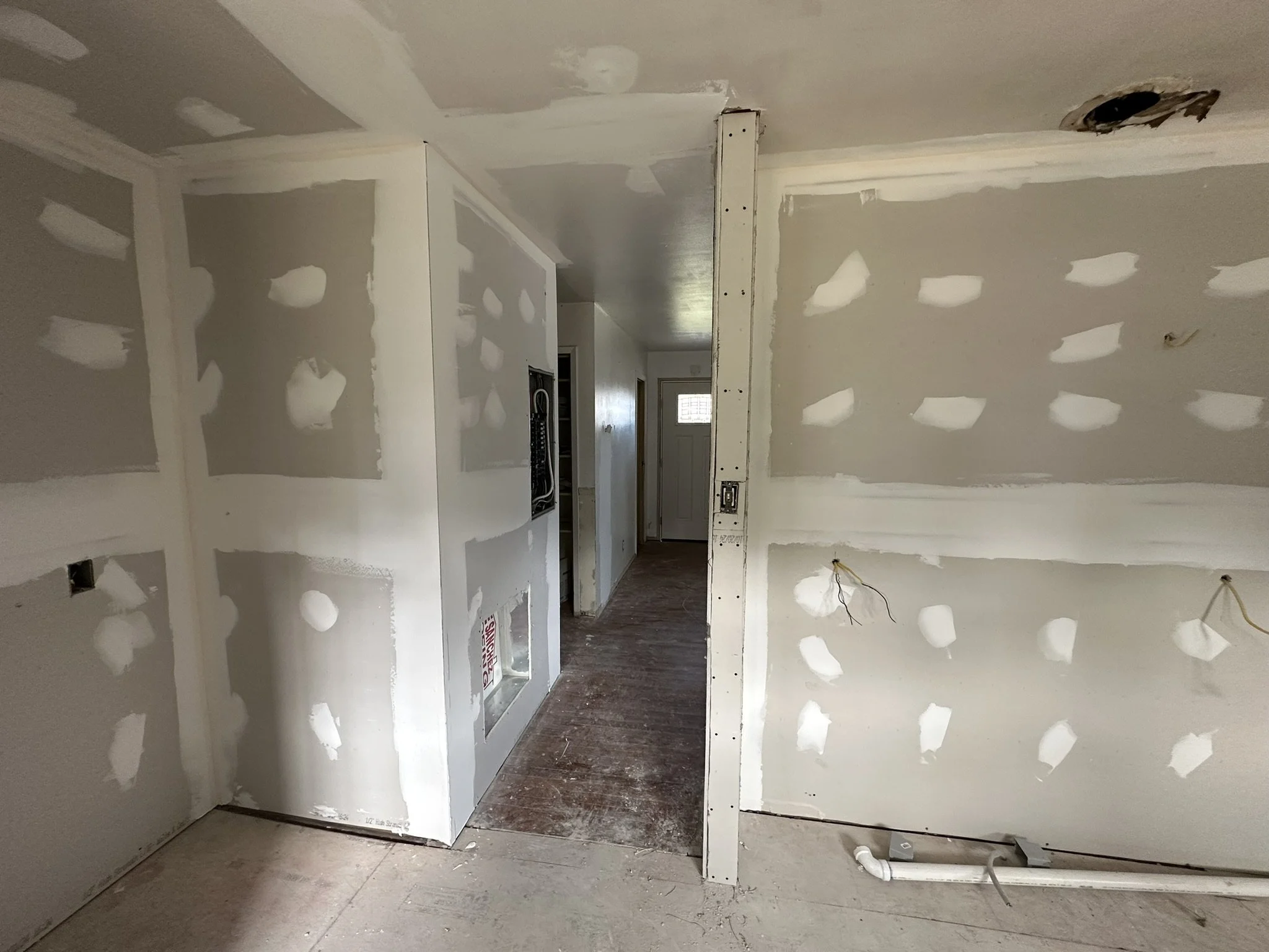Interior view of a house under construction with drywall, patches, electrical wires, and an open electrical panel.