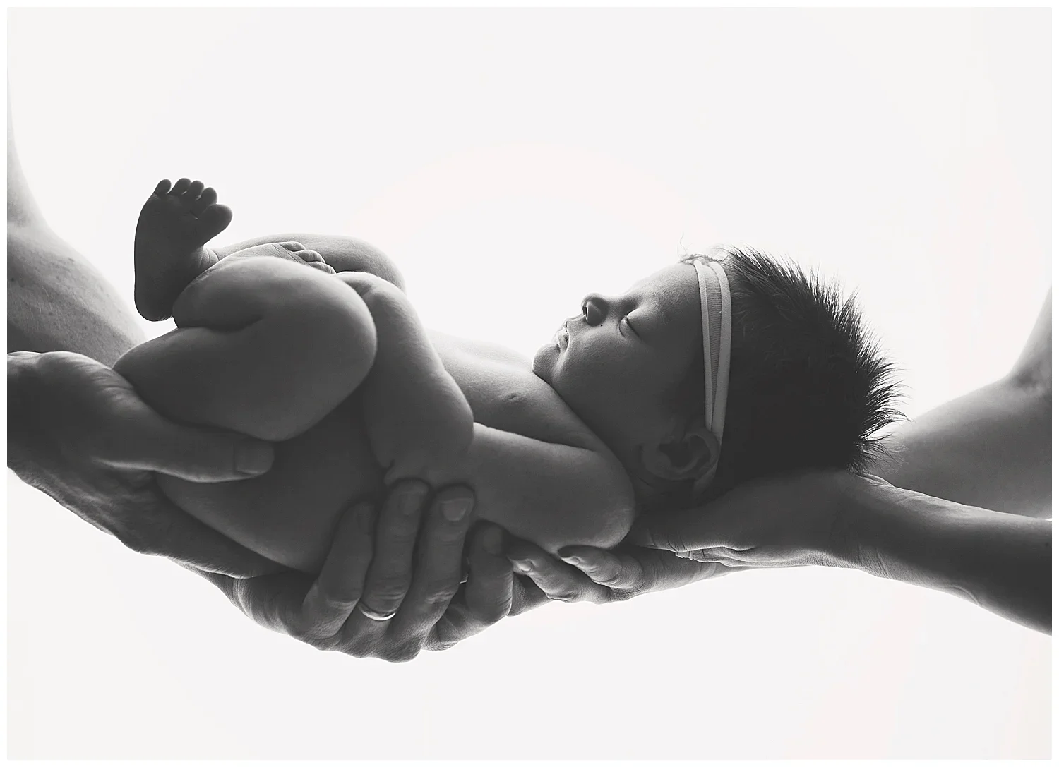 Black and white photo of a newborn baby being gently held by two adult hands, with a soft background.