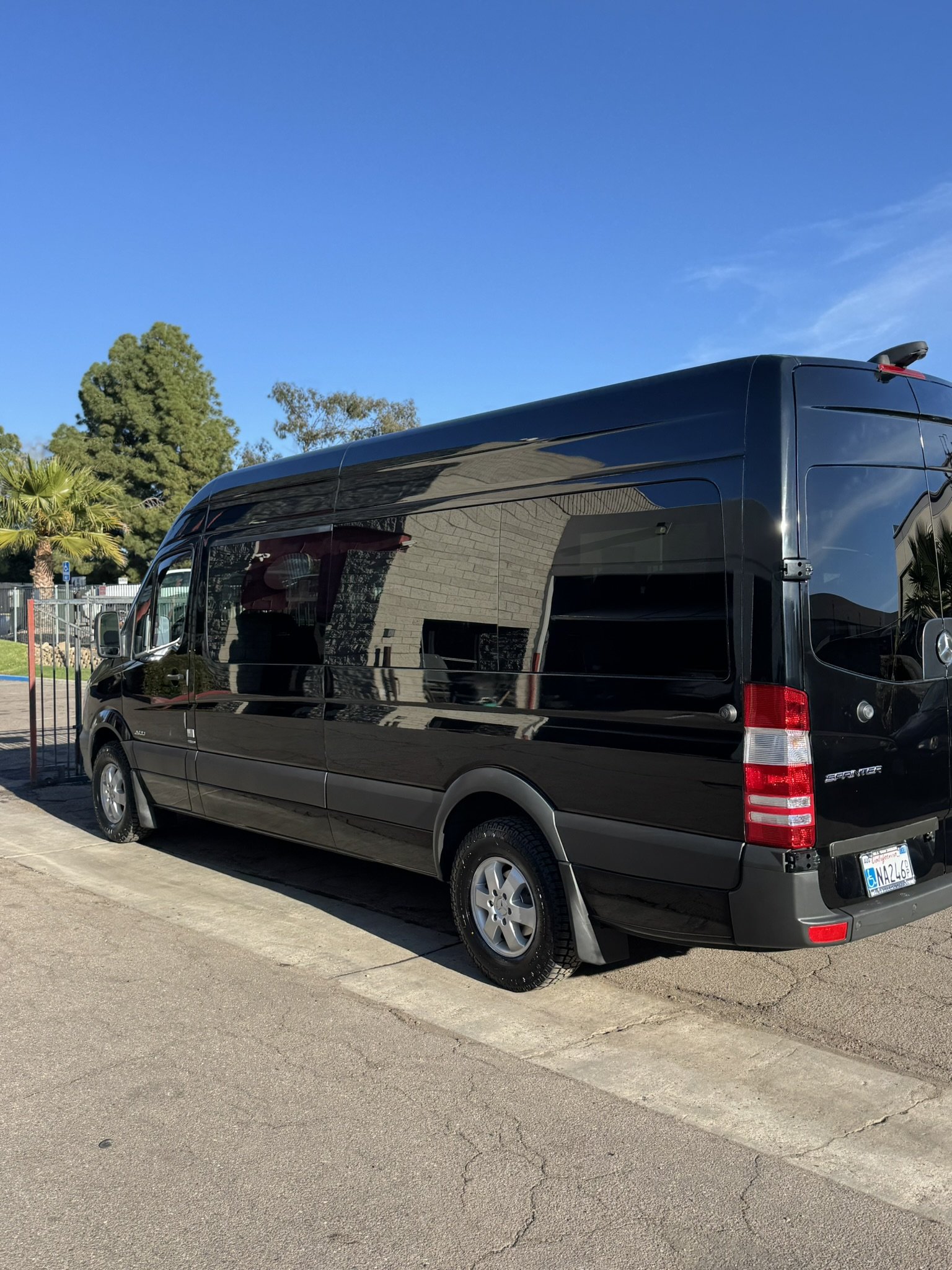 Black Mercedes-Benz Sprinter van parked on a street under clear blue sky.