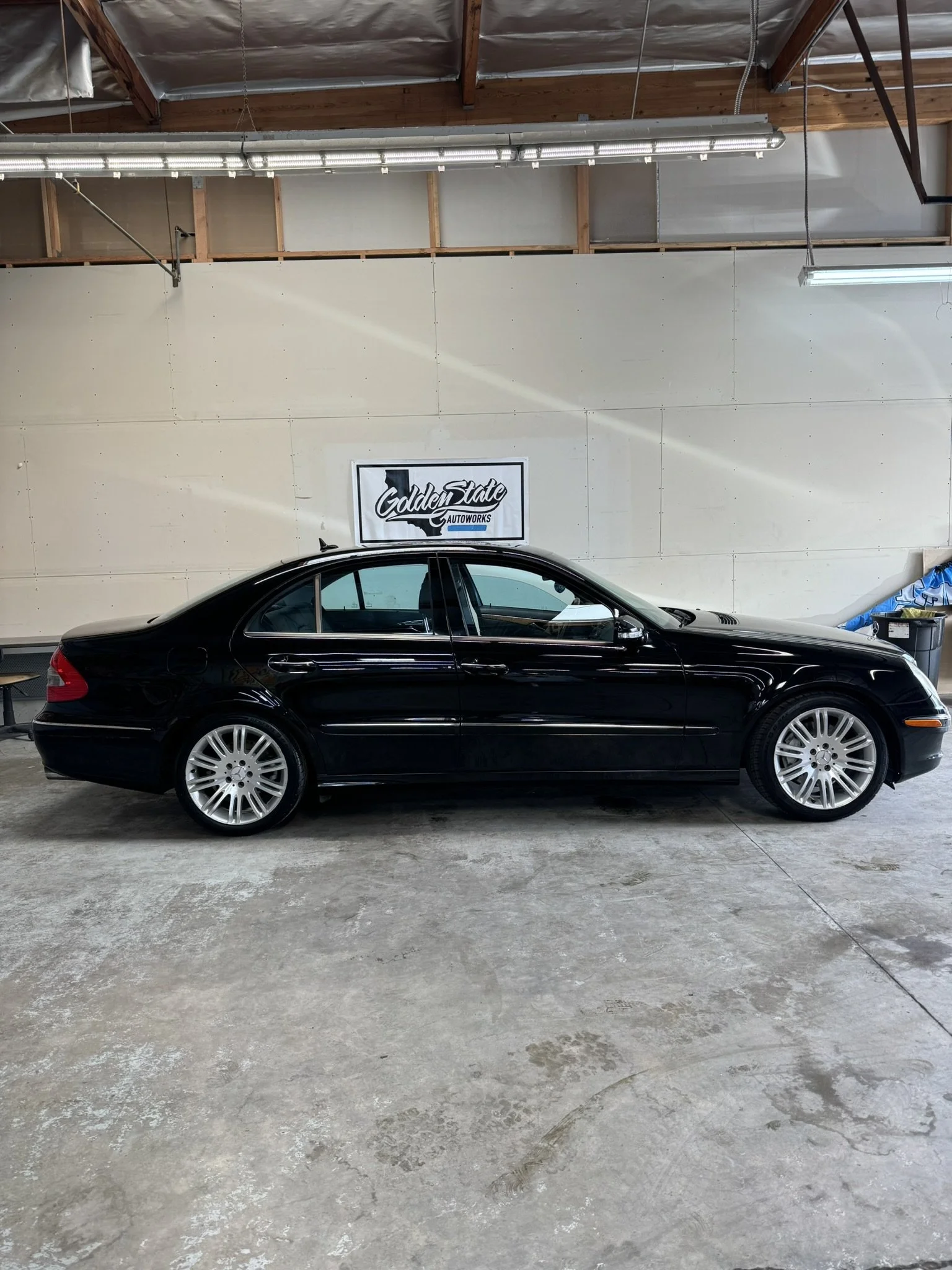 Black sedan parked inside an automotive workshop with a "Golden State Autoworks" sign on the wall.